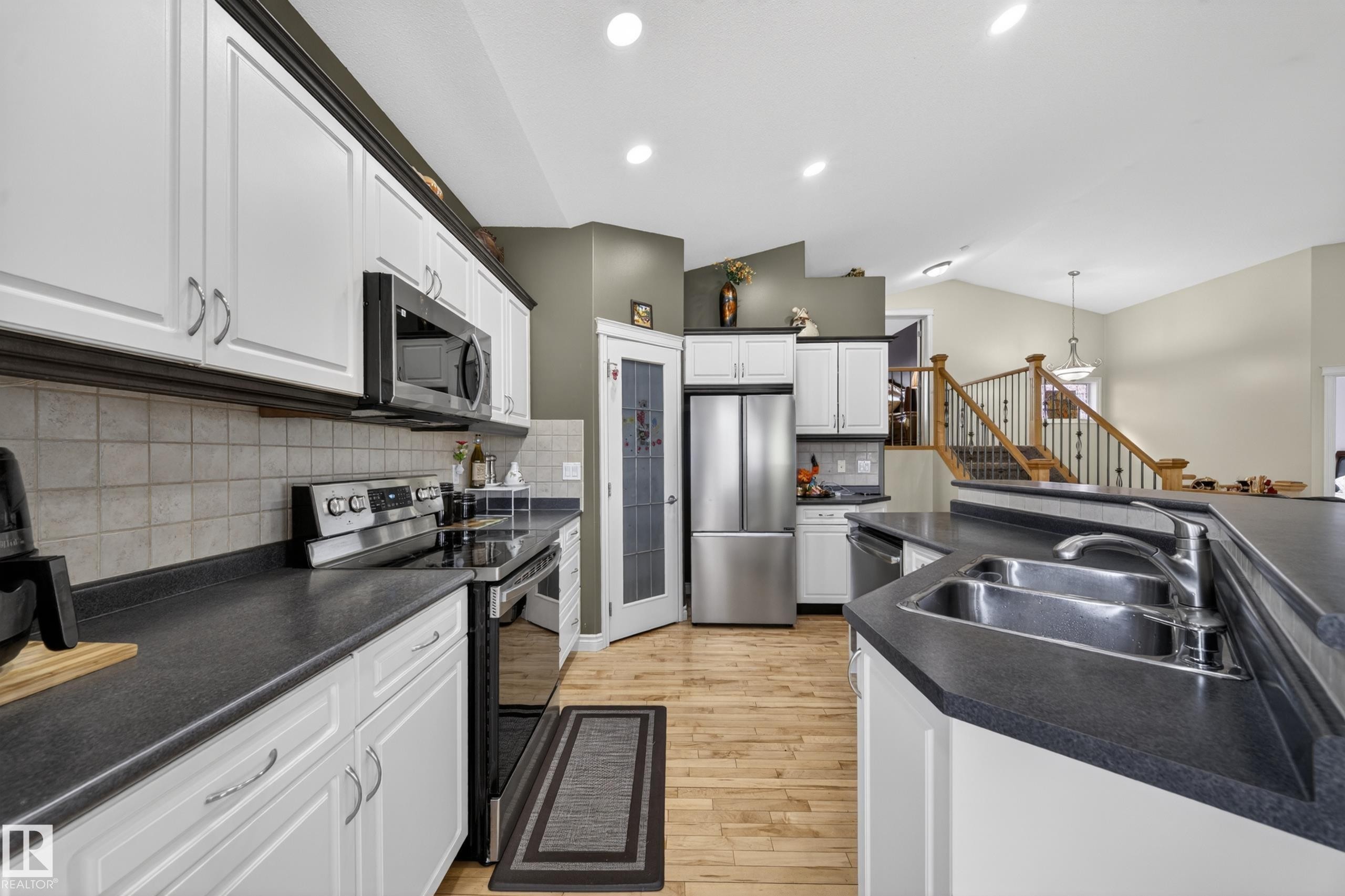 Spacious kitchen featuring white cabinetry, dark countertops, stainless steel appliances, a tile backsplash, and wood-finish flooring - 4113 59 Street, Beaumont, AB