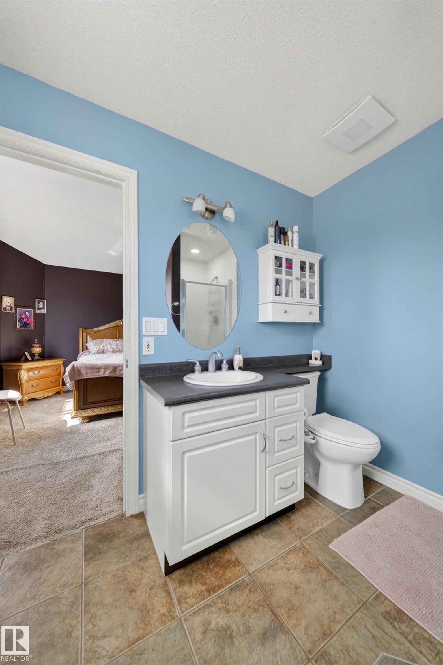 Bathroom featuring floor tiles, a white vanity with a countertop, an undermount sink, a wall-mounted mirror, and a toilet - 4113 59 Street, Beaumont, AB