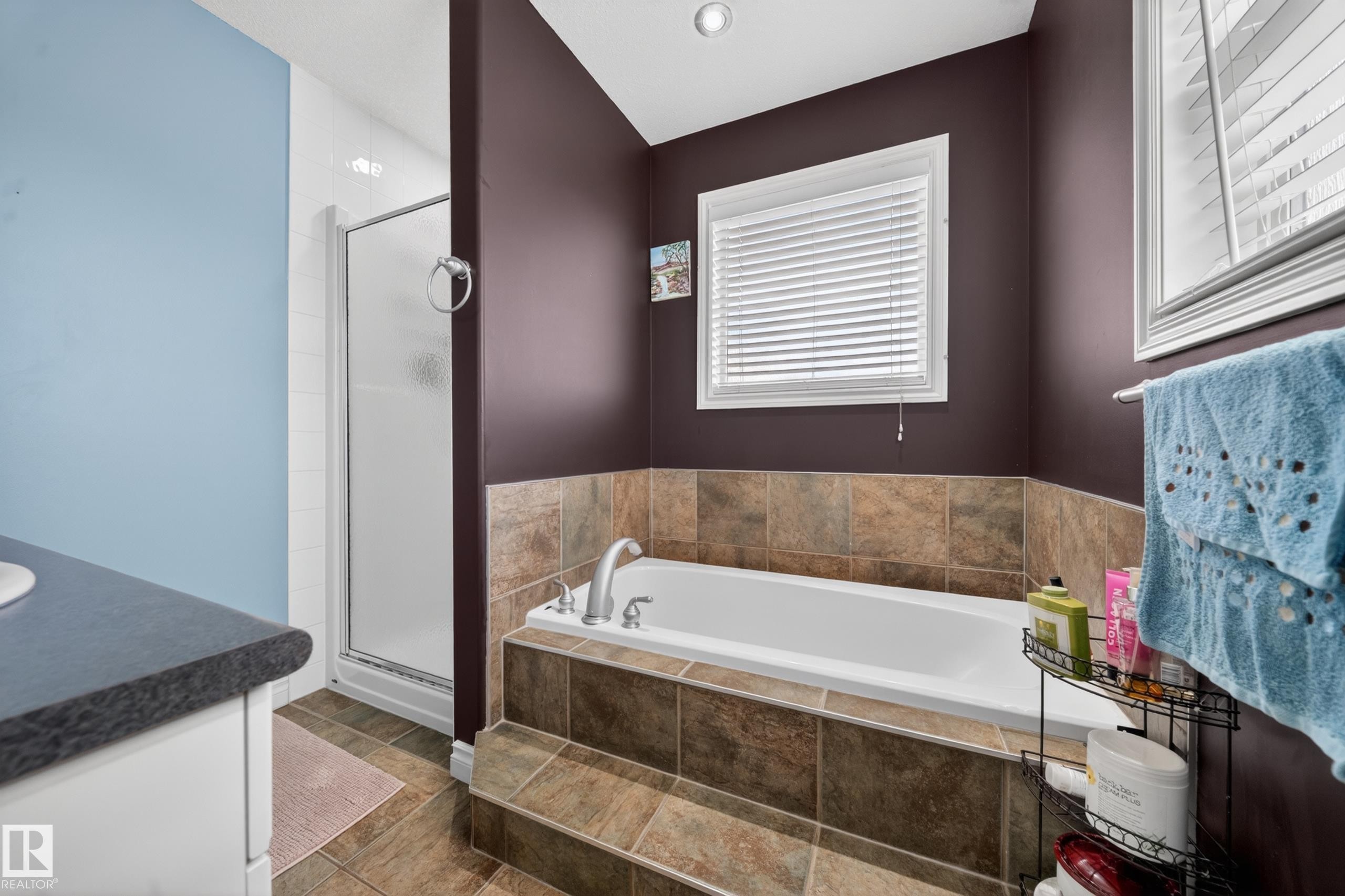 Bathroom featuring a built-in tub with tiled surround, a separate glass-enclosed shower, a vanity with a dark countertop, and an overhead recessed light - 4113 59 Street, Beaumont, AB