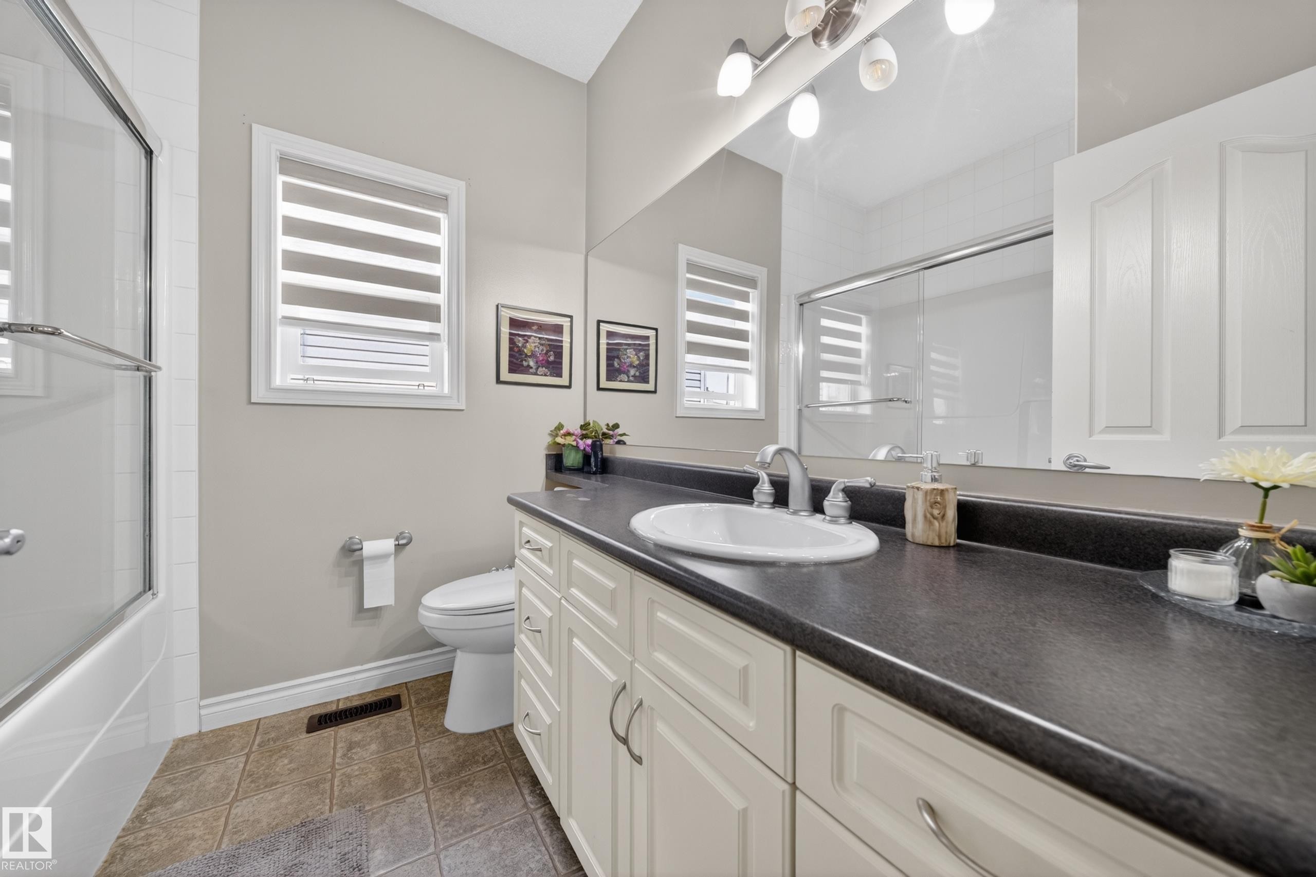 Bathroom featuring an extended vanity with a dark countertop, an integrated sink with a chrome faucet, and white paneled cabinetry - 4113 59 Street, Beaumont, AB