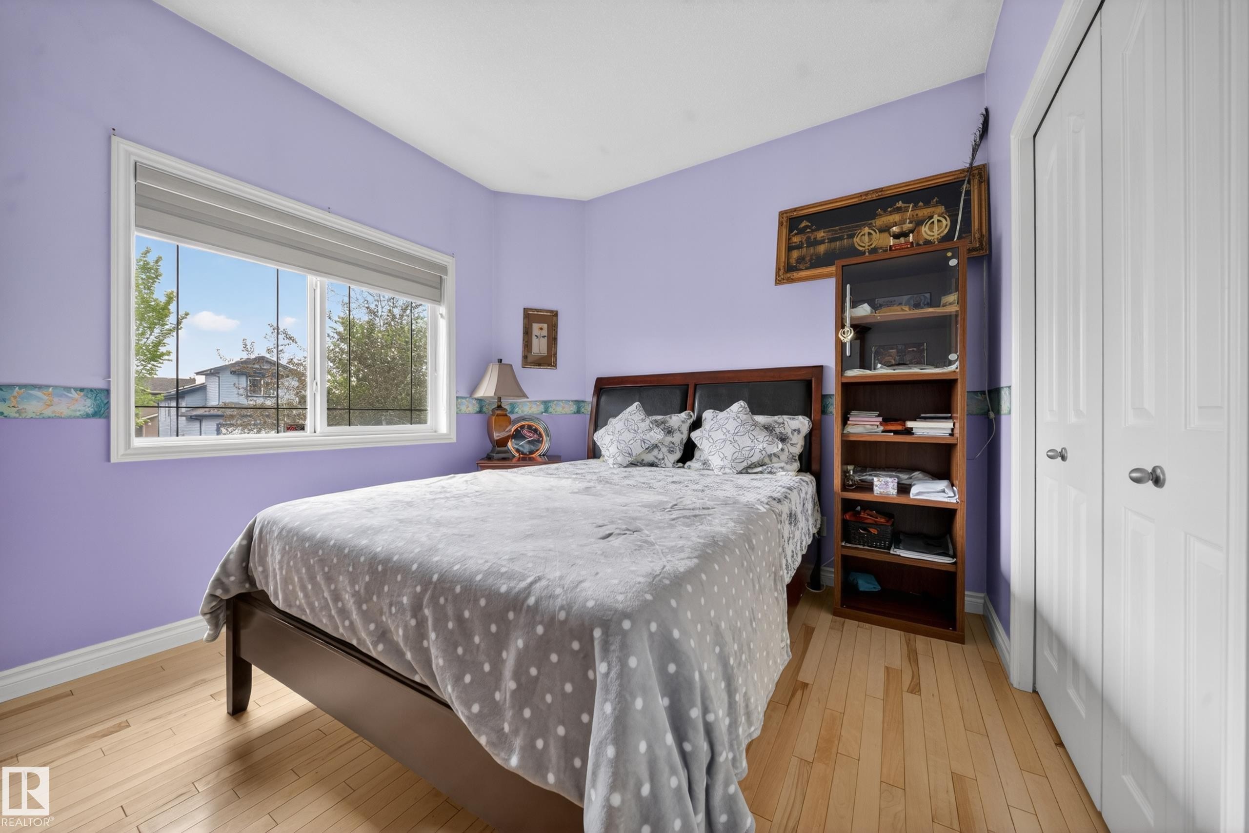 Bedroom featuring light wood-finish flooring, a large window with white trim, and a bi-fold closet with white paneled doors - 4113 59 Street, Beaumont, AB