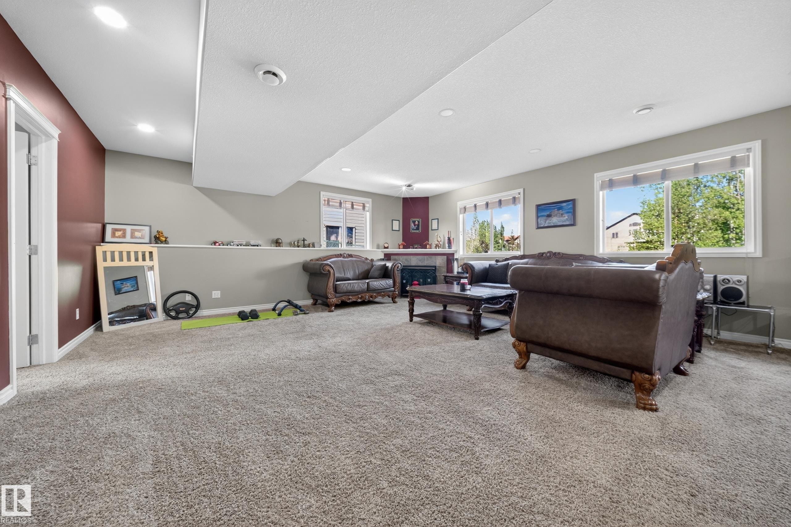 Spacious carpeted room featuring recessed lighting, multiple windows, a built-in fireplace, and a partial wall defining the space - 4113 59 Street, Beaumont, AB