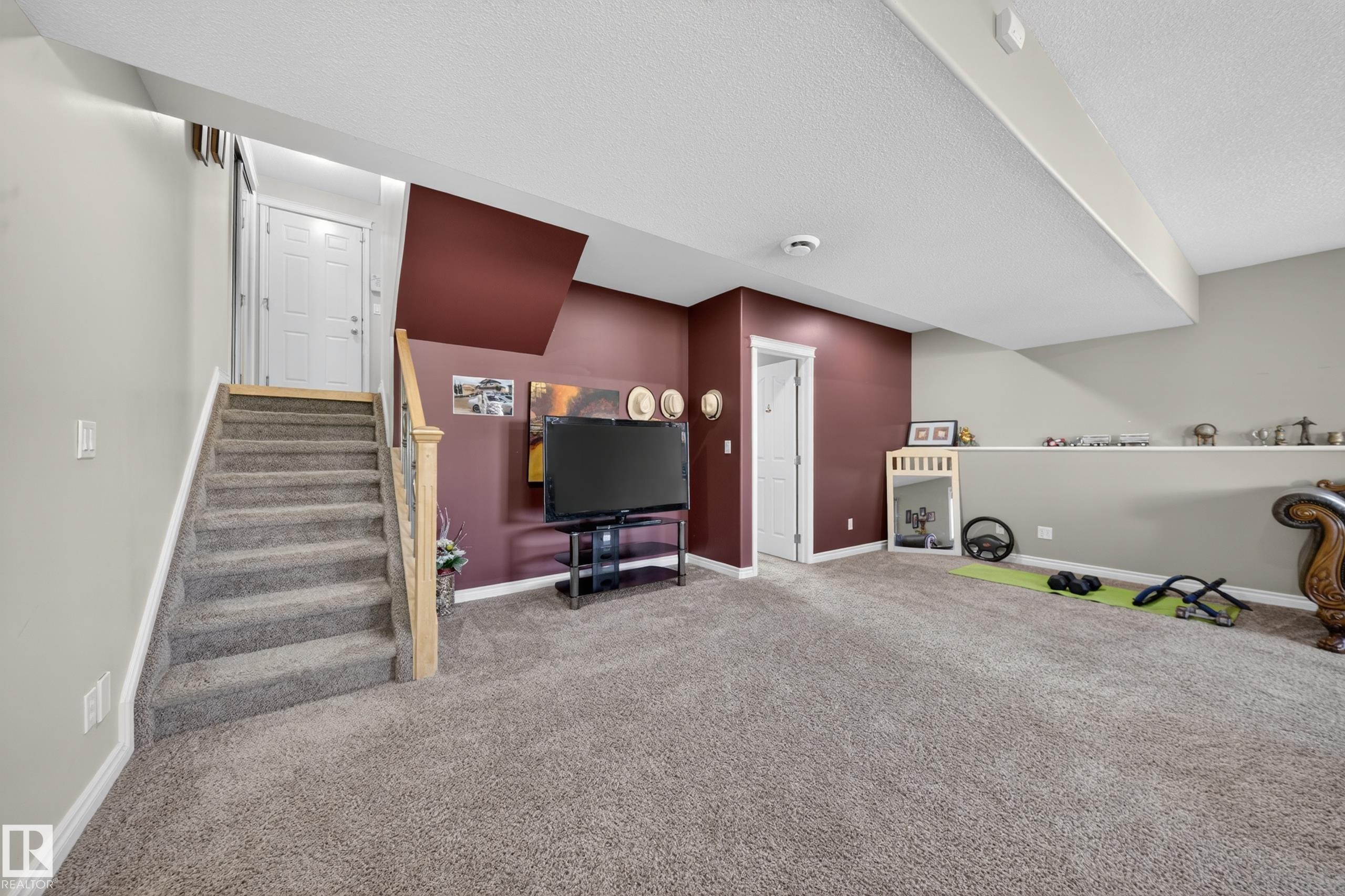 Carpeted lower level featuring a staircase with light wood newel posts, a white paneled door, and a built-in shelf along one wall - 4113 59 Street, Beaumont, AB