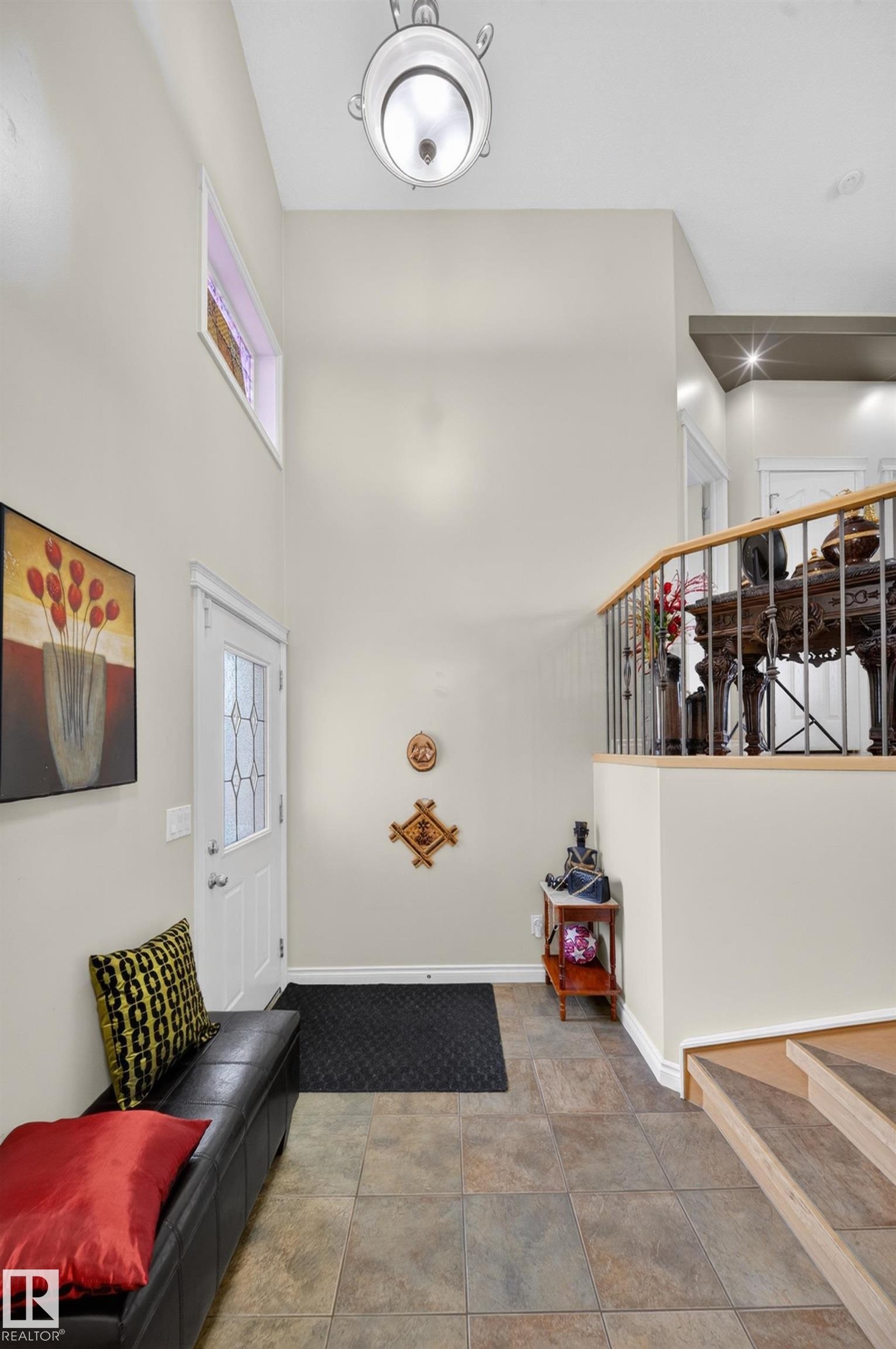 Foyer featuring multi-toned tile flooring, a white paneled entry door with decorative glass inserts, and a high ceiling with a mounted light fixture - 4113 59 Street, Beaumont, AB