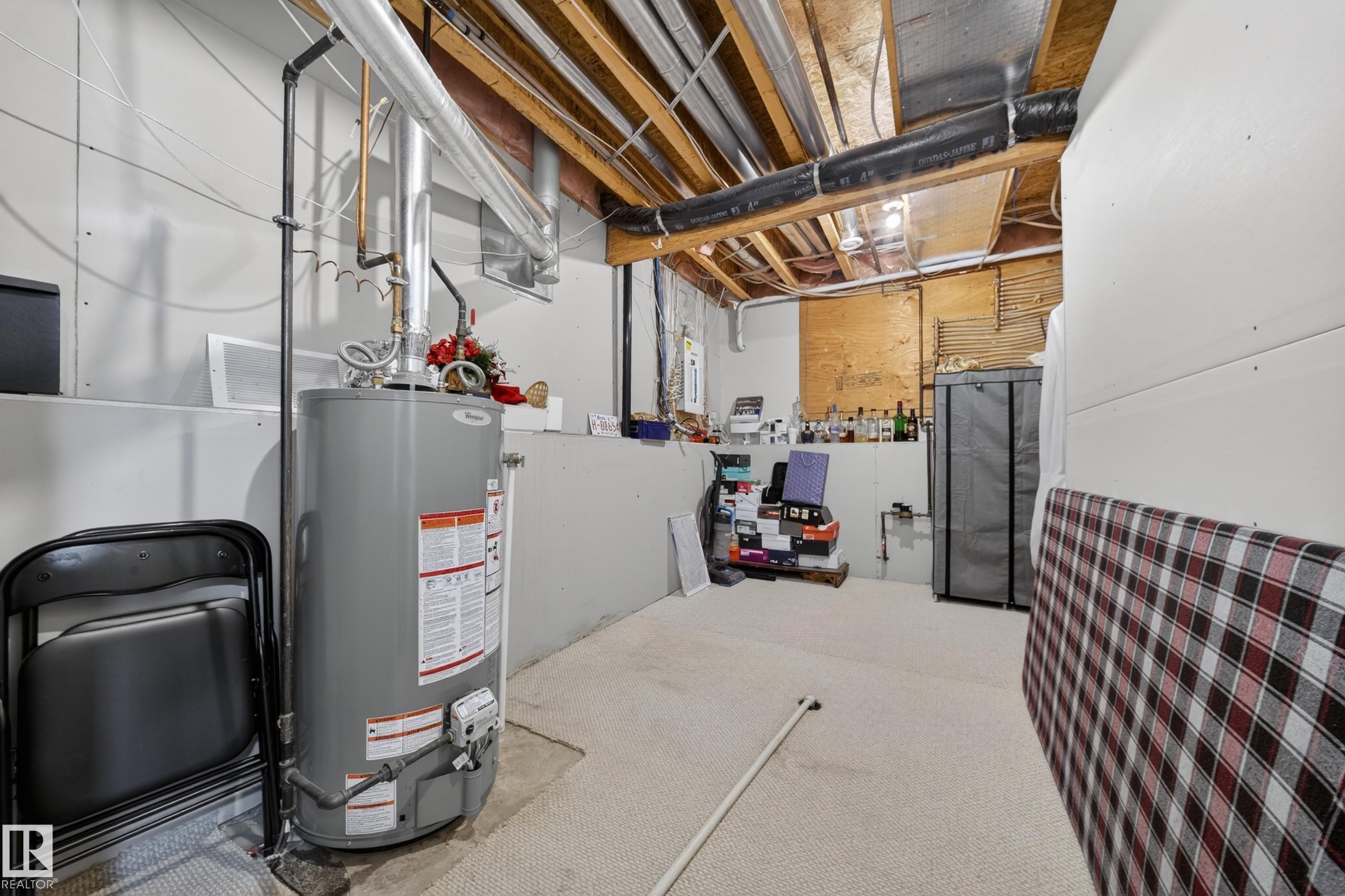 Utility room with exposed ceiling joists and ductwork, featuring a water heater, carpeted flooring, and partially finished walls - 4113 59 Street, Beaumont, AB