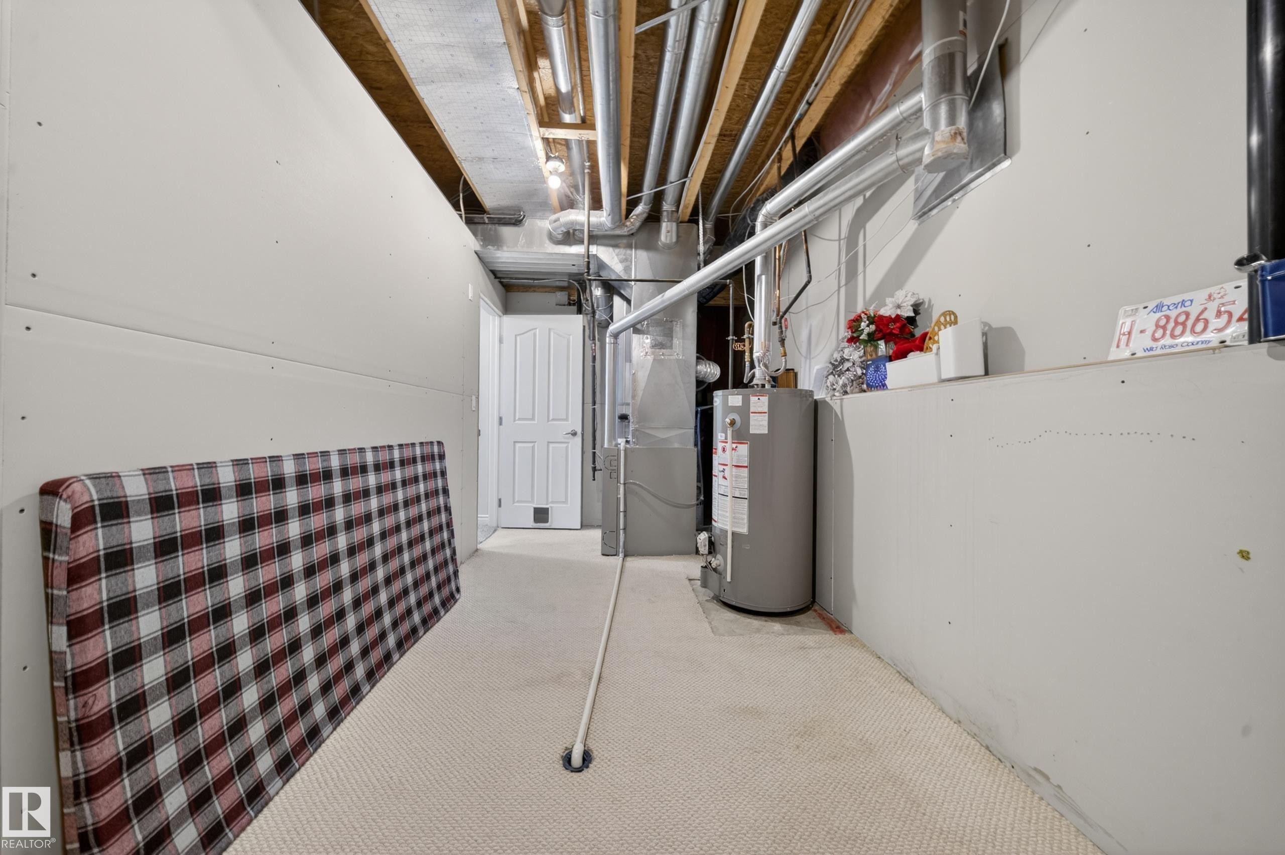 Unfinished utility space featuring a water heater, exposed ceiling joists and ductwork, a paneled door with a pet door, and carpeting - 4113 59 Street, Beaumont, AB