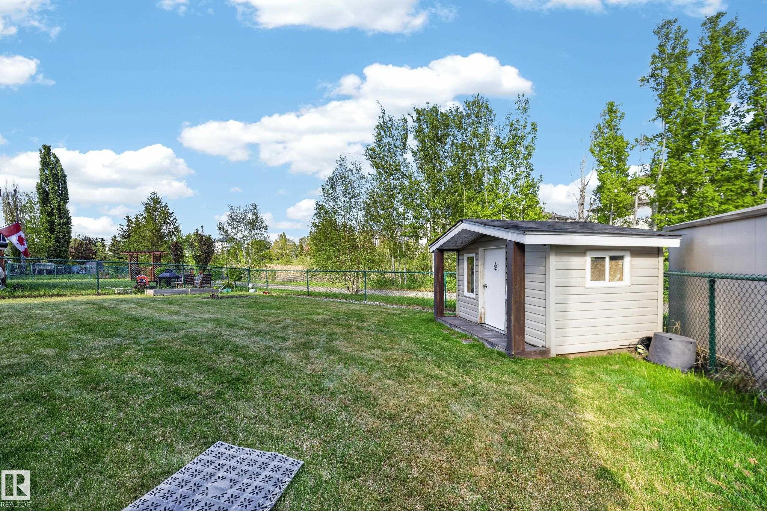 Expansive backyard featuring a storage shed with siding, a chain-link fence, and mature trees - 4113 59 Street, Beaumont, AB