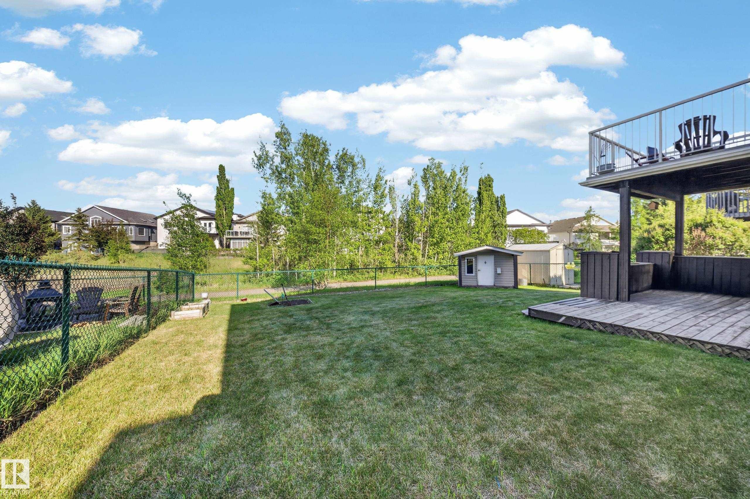 Expansive backyard featuring a lush lawn, chain link fencing, and a detached storage shed - 4113 59 Street, Beaumont, AB