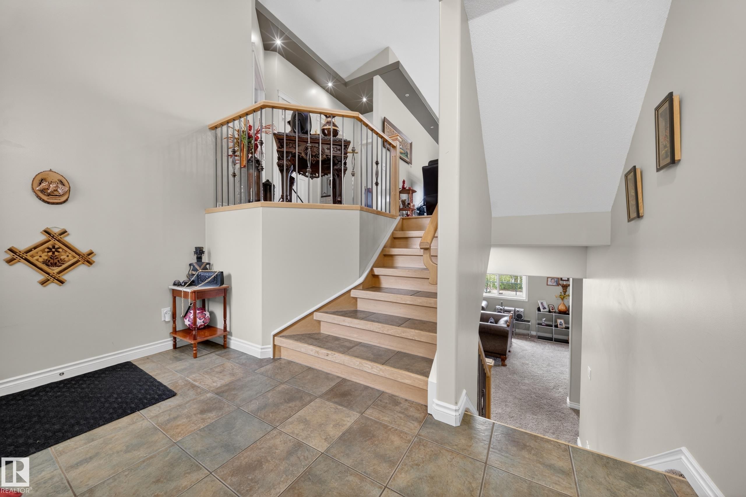 Entryway featuring tile flooring, a staircase with wood-finish treads and a wood and metal railing, and a lower-level living area with carpeting - 4113 59 Street, Beaumont, AB