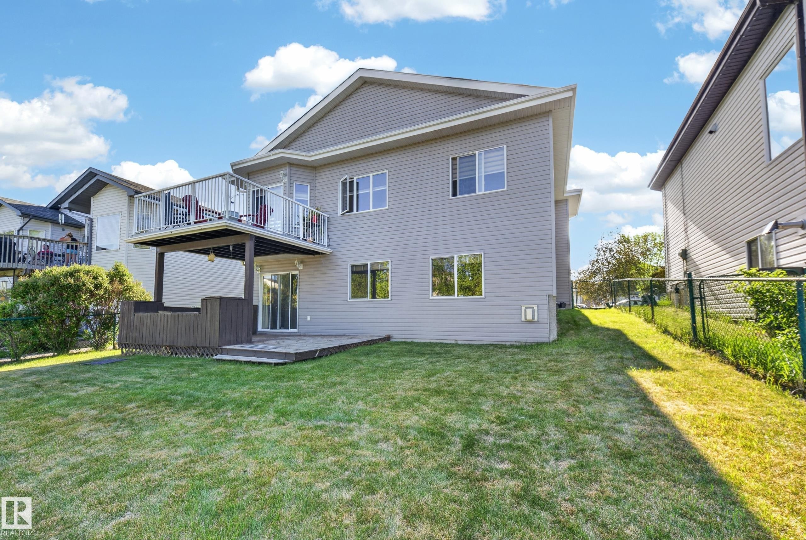 Rear elevation featuring a multi-level deck system with metal railings, a lower-level patio, and a spacious grassy area - 4113 59 Street, Beaumont, AB