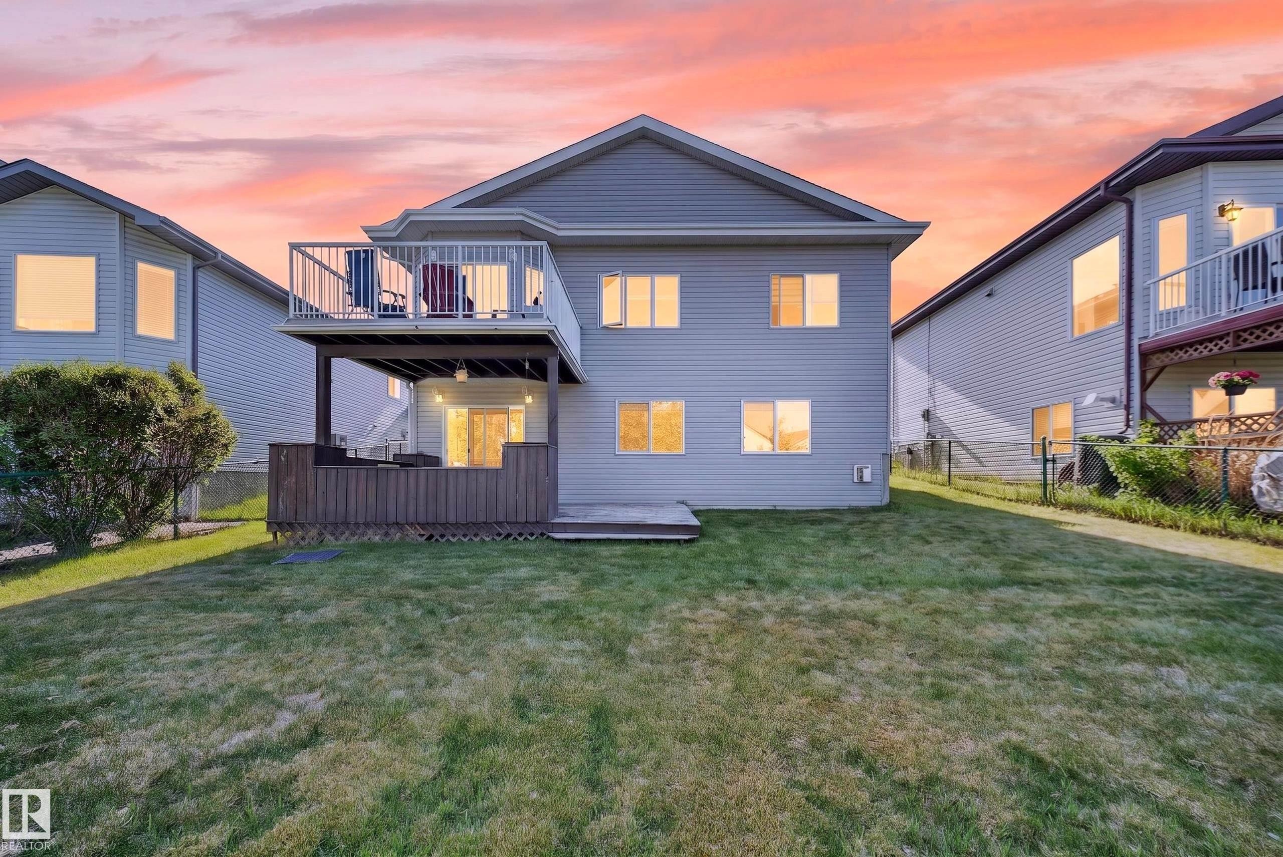Expansive grass lawn at the rear of the property featuring a raised deck with white railing, covered patio below, and sliding glass doors - 4113 59 Street, Beaumont, AB