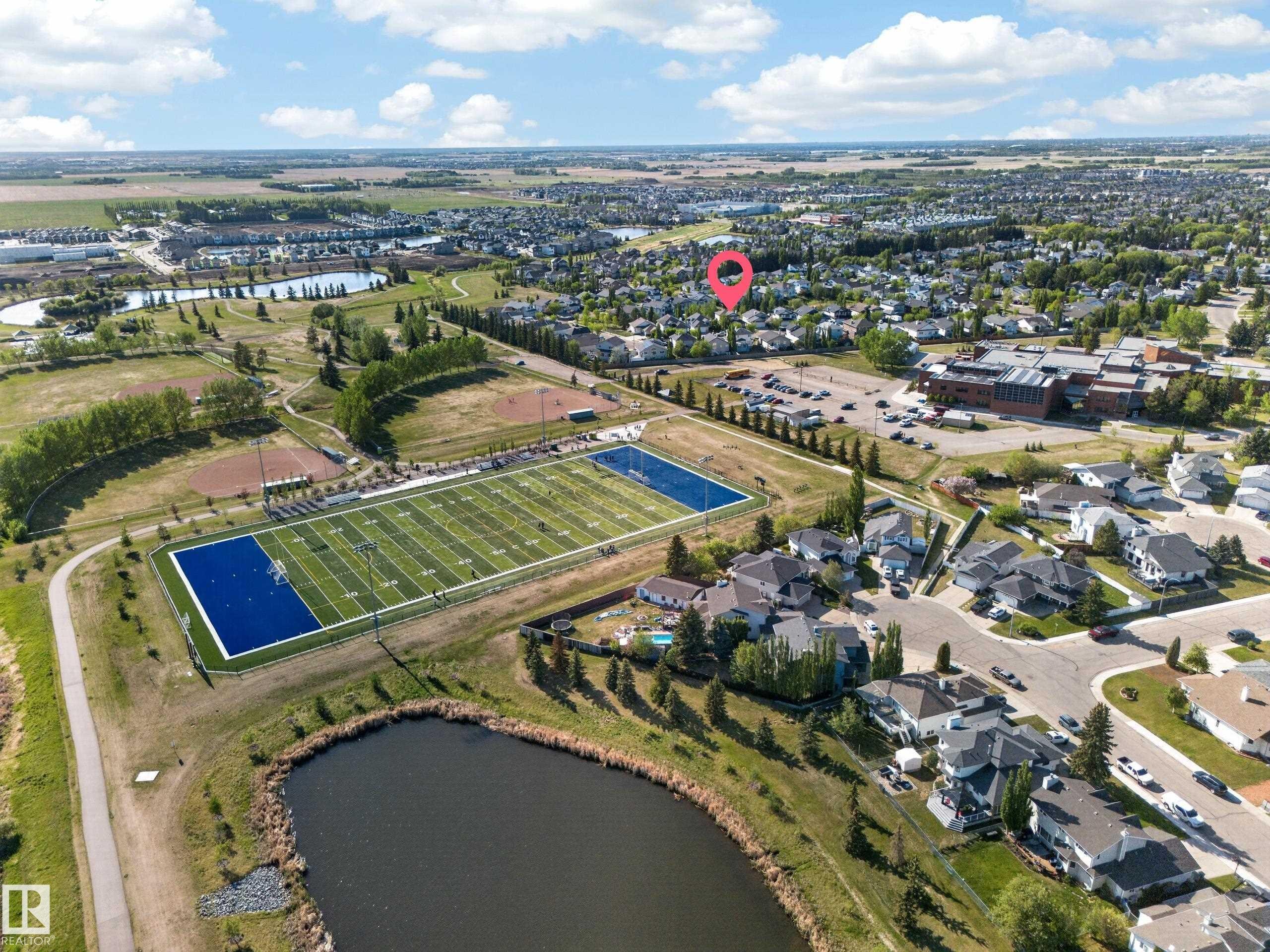 Aerial perspective showcasing the surrounding community, including a sports field, a body of water, and residential homes - 4113 59 Street, Beaumont, AB