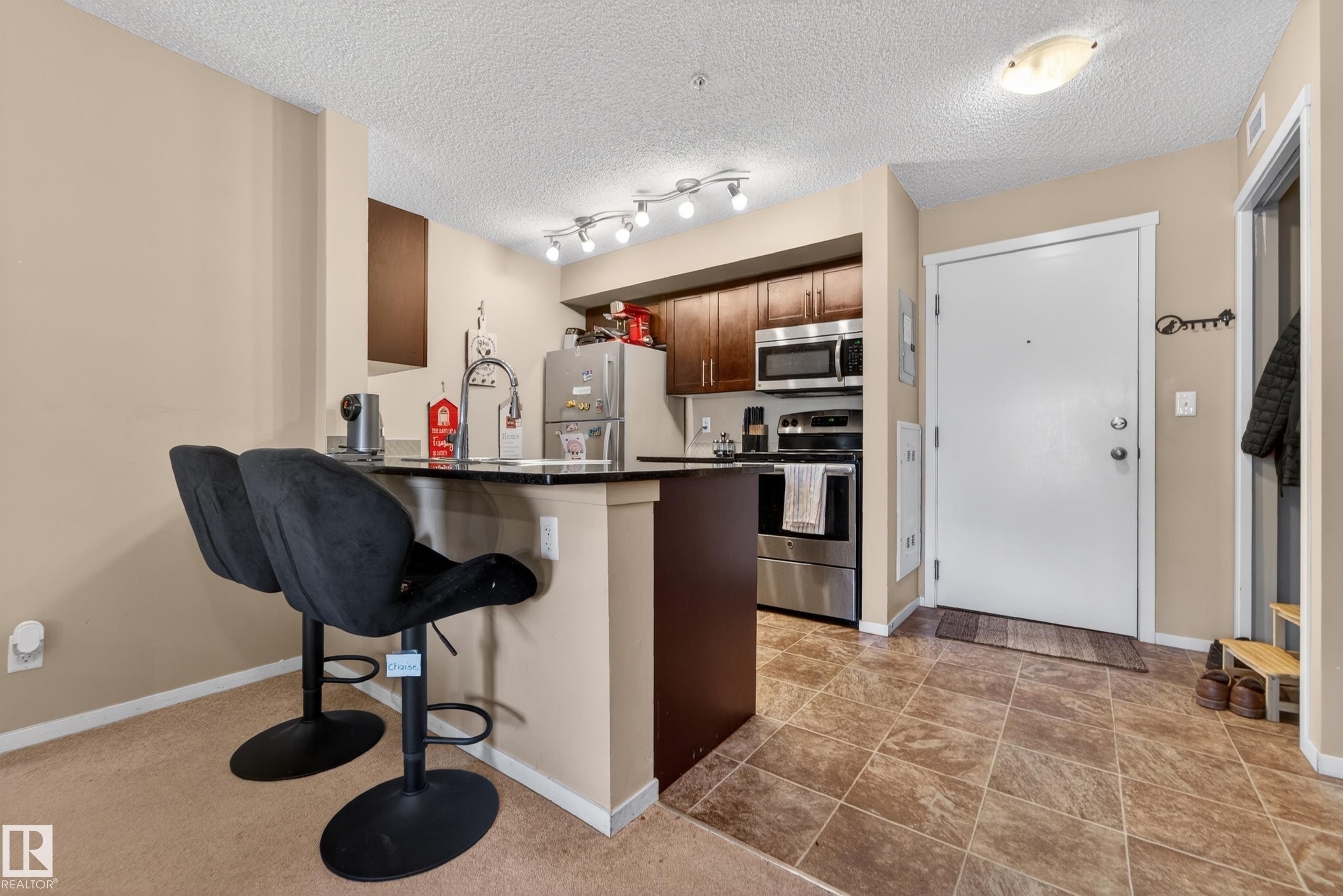 Kitchen with dark wood cabinetry, stainless steel appliances, and a breakfast bar featuring a black countertop - 225 1510 Watt Drive, Edmonton, AB - Indoor Photo Showing Kitchen