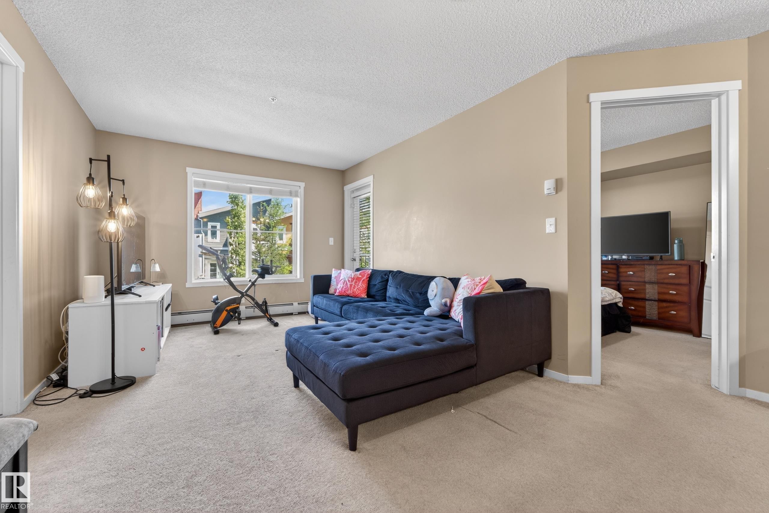 Spacious living area featuring neutral-toned walls, light-colored carpeting, and a large window providing natural light - 225 1510 Watt Drive, Edmonton, AB - Indoor Photo Showing Living Room