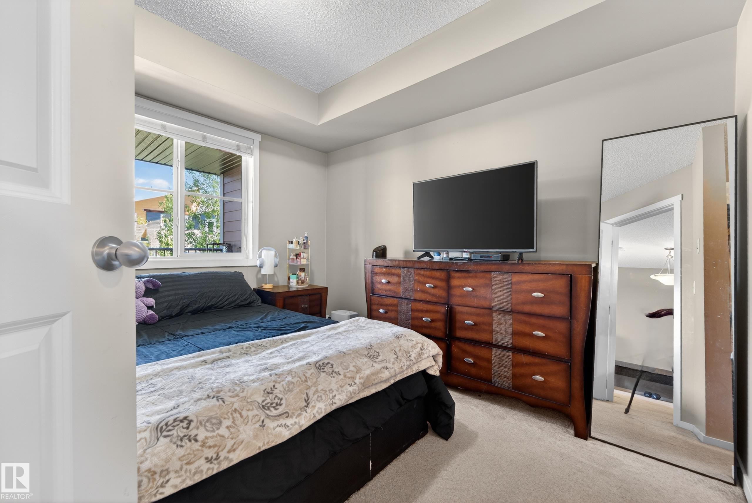 Bedroom featuring light neutral walls, a window with horizontal blinds, and a tray ceiling detail - 225 1510 Watt Drive, Edmonton, AB - Indoor Photo Showing Bedroom