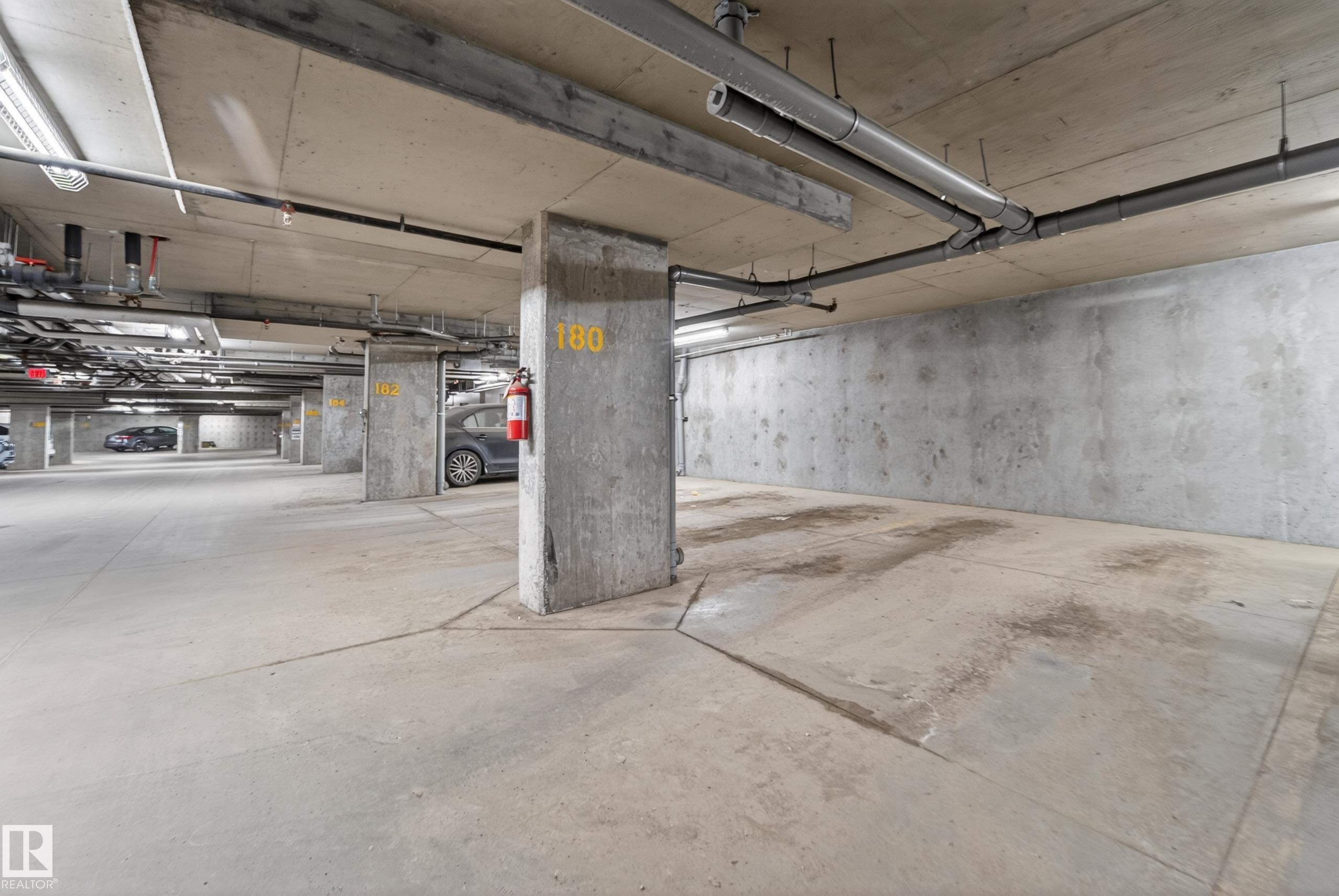 Concrete subterranean parking area featuring exposed ceiling utilities and structural columns - 225 1510 Watt Drive, Edmonton, AB - Indoor Photo Showing Garage