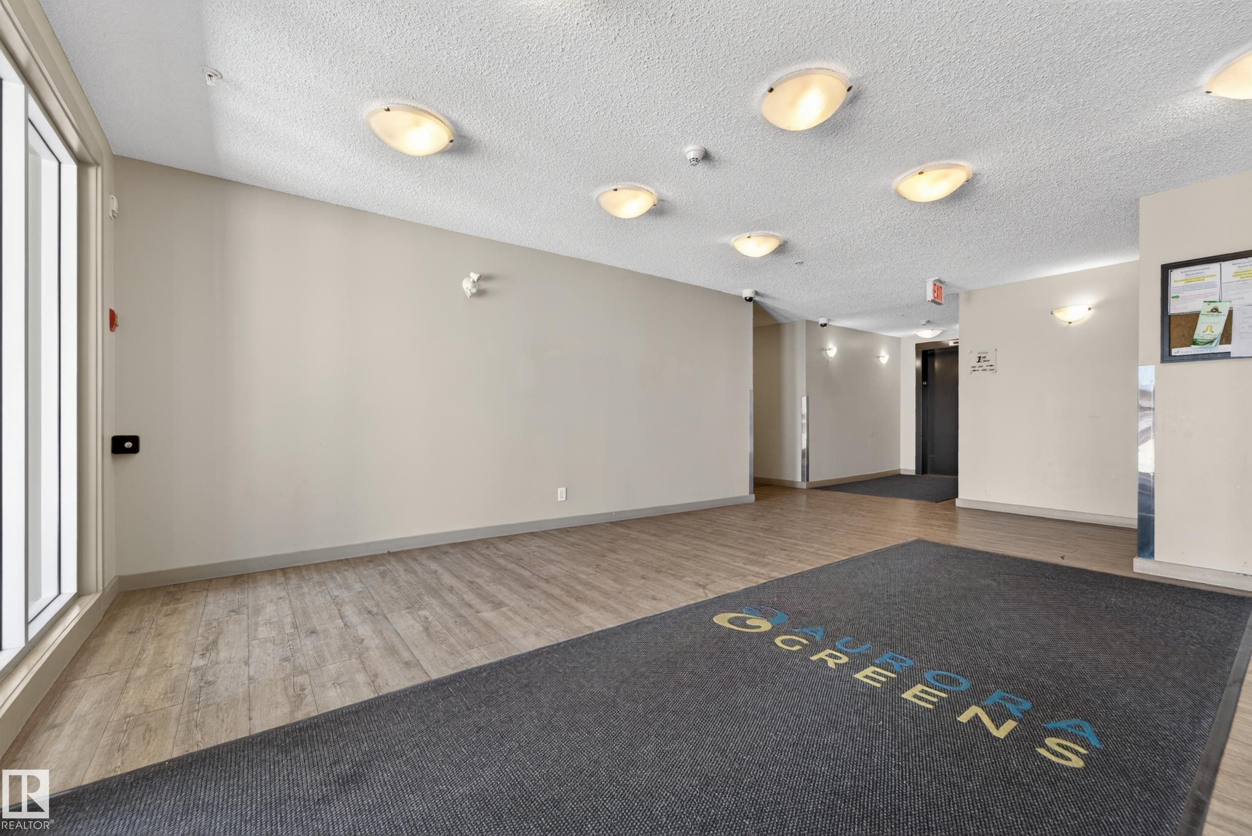 Entryway featuring wood-finish flooring, neutral wall tones, multiple ceiling-mounted light fixtures, and a glass-paneled exterior door - 225 1510 Watt Drive, Edmonton, AB - Indoor Photo Showing Other Room