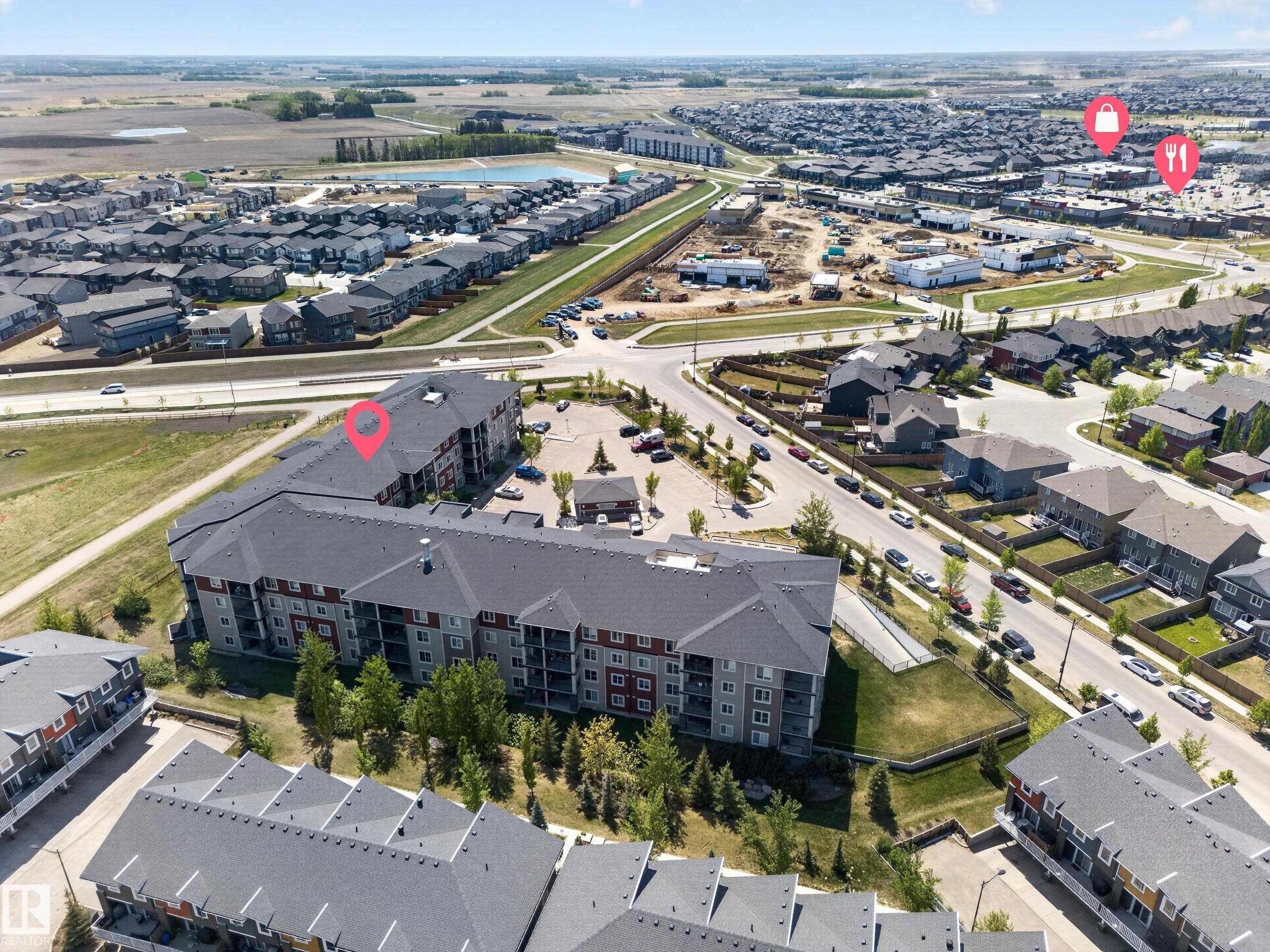 Multi-story residential building with gray siding and red accents, featuring multiple balconies and a large parking area - 225 1510 Watt Drive, Edmonton, AB - Outdoor With View