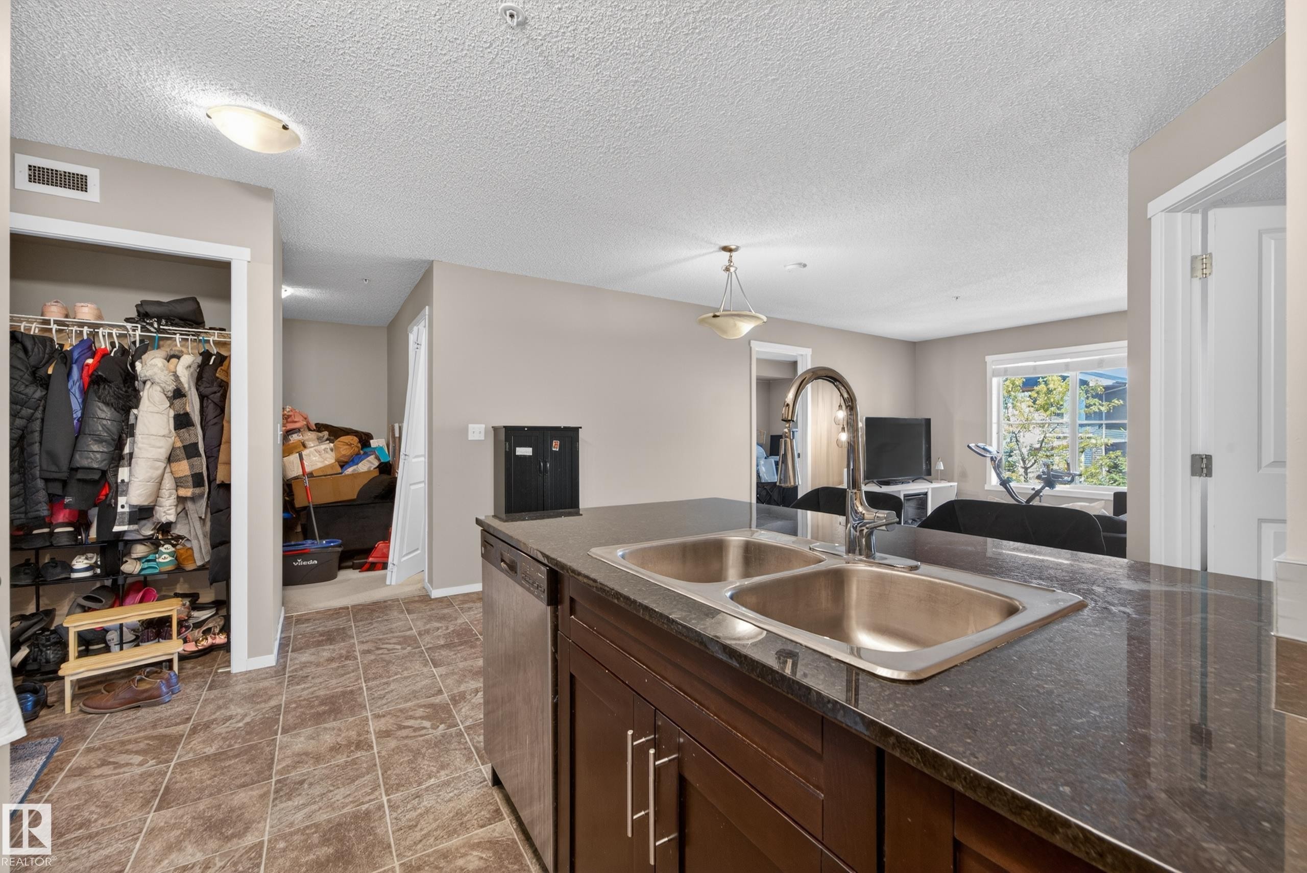 Kitchen island with a double stainless steel sink, gooseneck faucet, and dark stone countertop - 225 1510 Watt Drive, Edmonton, AB - Indoor Photo Showing Kitchen With Double Sink