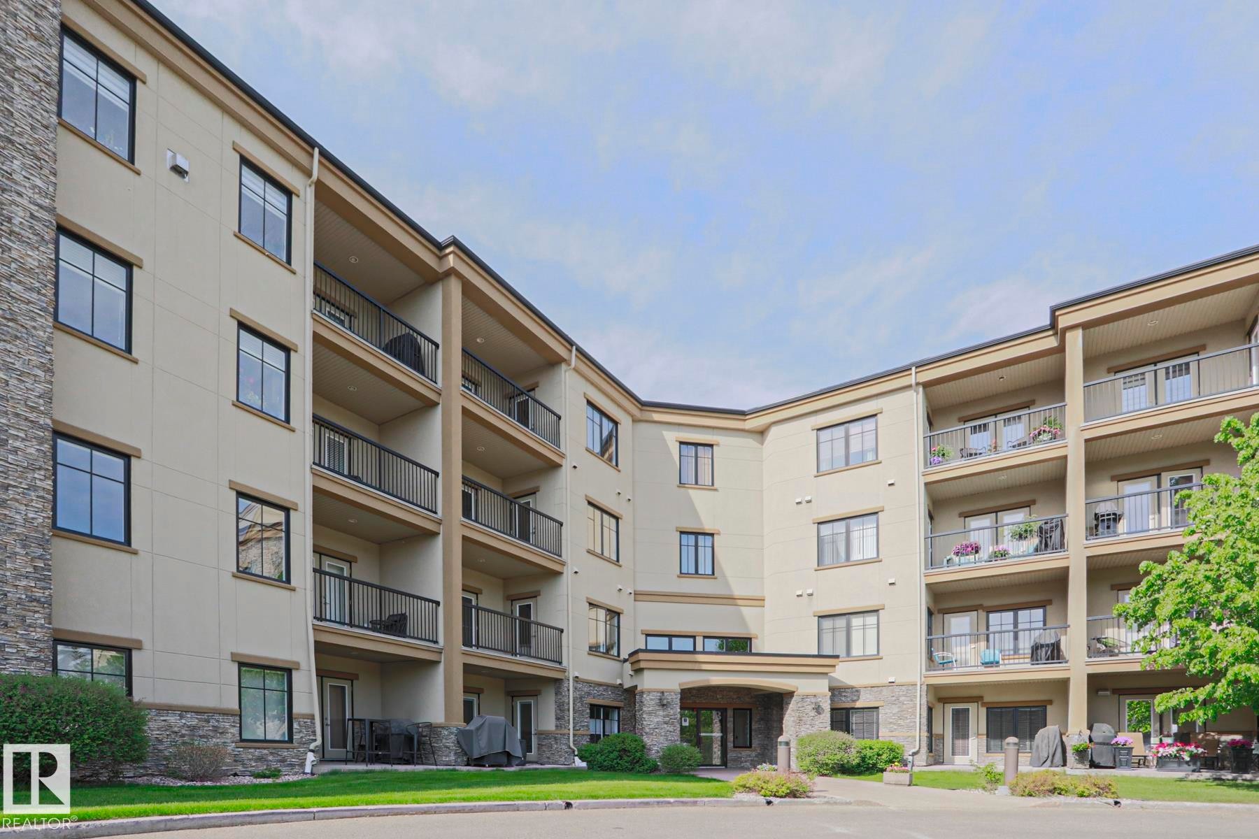 Multi-story residential building featuring a stucco exterior with stone accents - 117 160 Magrath Road, Edmonton, AB - Outdoor With Facade