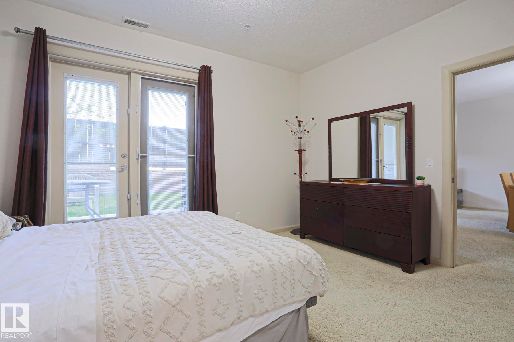Carpeted room with double glass-paneled doors opening to an exterior patio - 117 160 Magrath Road, Edmonton, AB - Indoor Photo Showing Bedroom