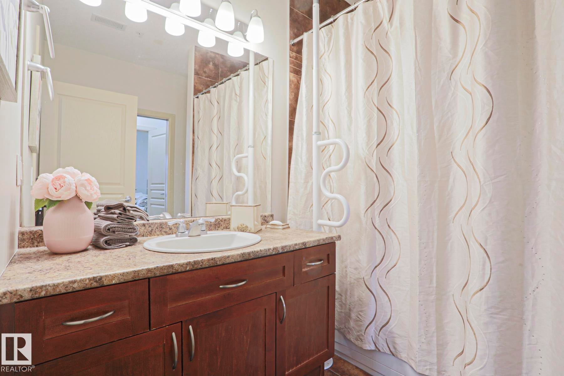 Vanity featuring a built-in sink, stone-look countertop, and dark wood cabinetry - 117 160 Magrath Road, Edmonton, AB - Indoor Photo Showing Bathroom