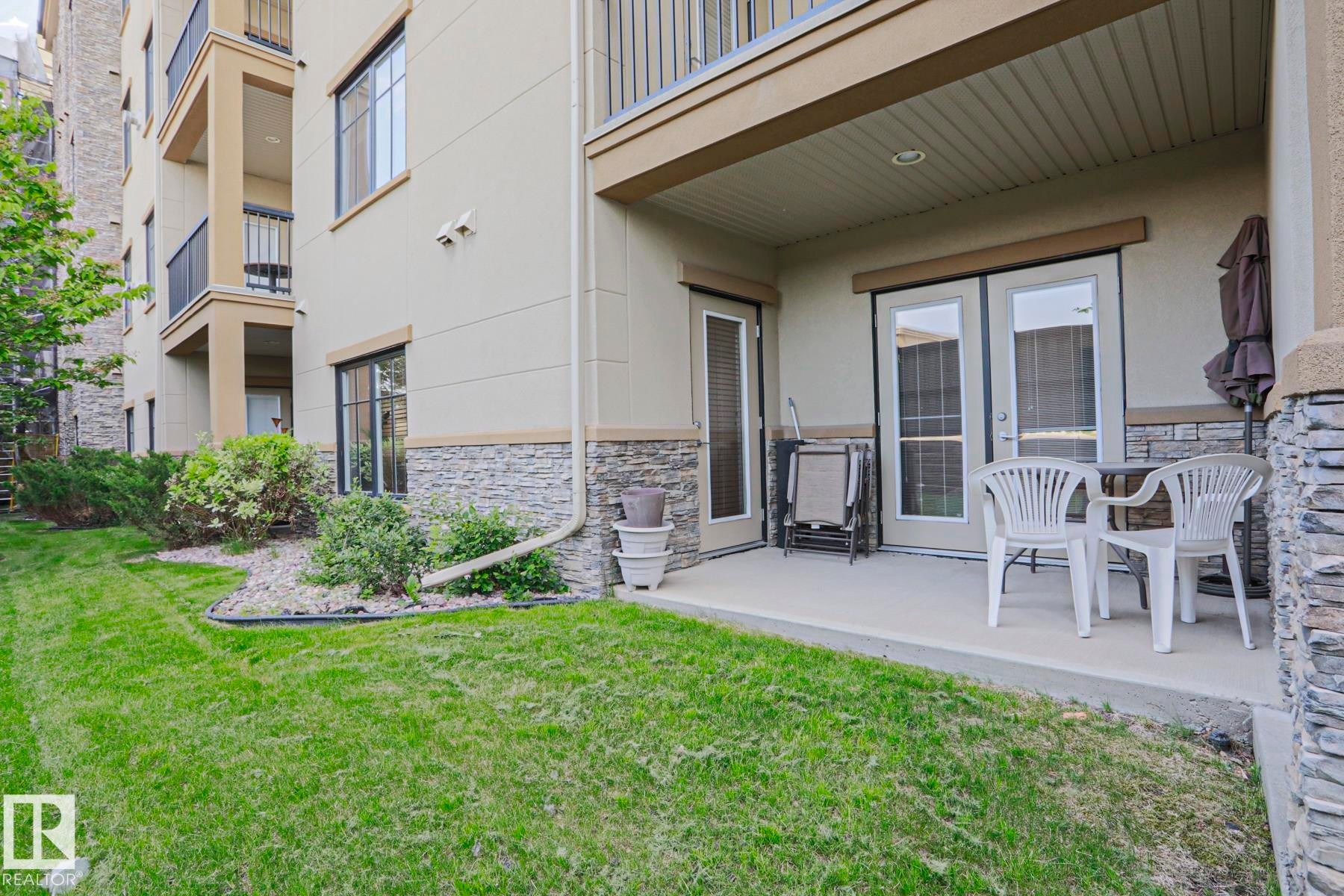 Ground-level patio featuring double French doors and stone veneer siding - 117 160 Magrath Road, Edmonton, AB - Outdoor With Deck Patio Veranda
