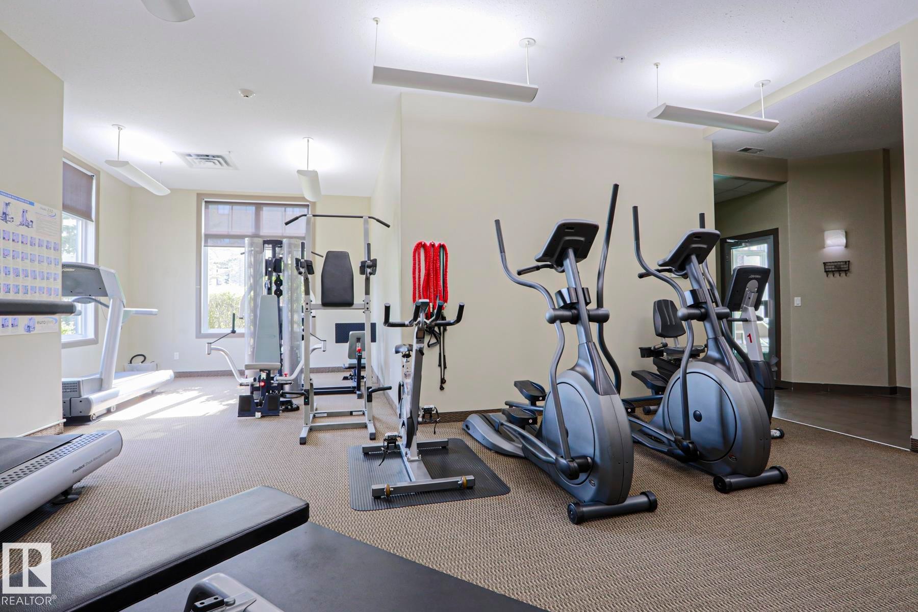 Dedicated fitness room featuring multiple exercise machines, expansive windows, carpet flooring, and recessed lighting - 117 160 Magrath Road, Edmonton, AB - Indoor Photo Showing Gym Room
