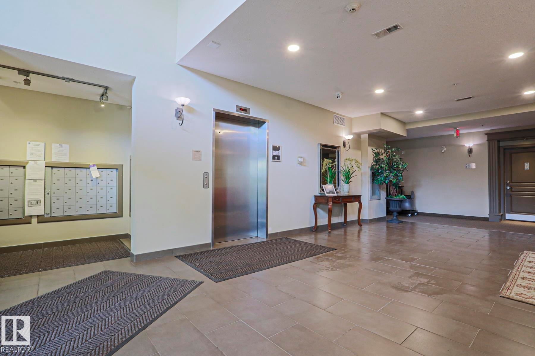 Lobby area featuring tile flooring, a stainless steel elevator, recessed lighting, and wall-mounted mailboxes - 117 160 Magrath Road, Edmonton, AB - Indoor Photo Showing Other Room