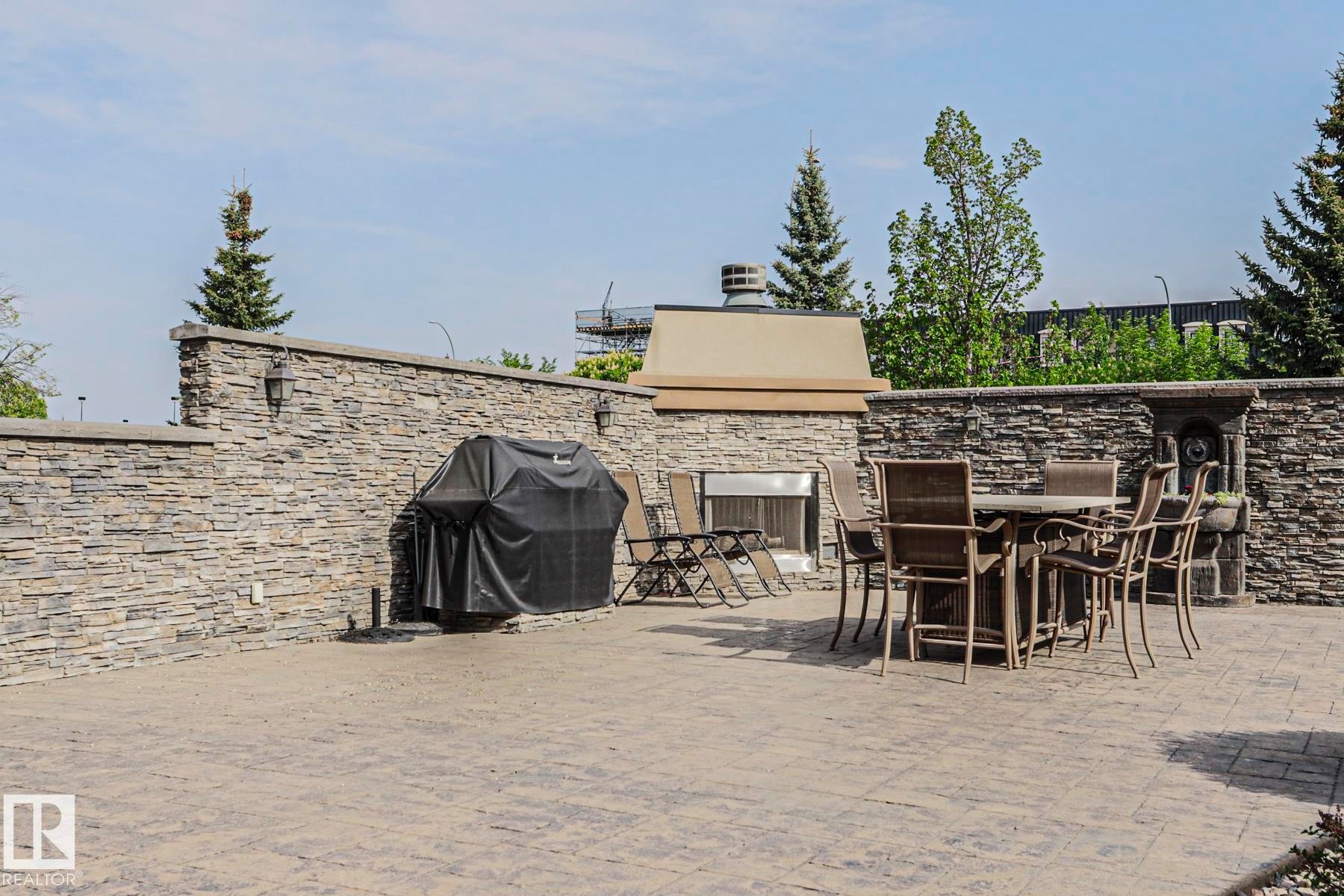 Expansive outdoor patio featuring stamped concrete flooring, stone veneer walls, a built-in outdoor fireplace, and integrated wall sconces - 117 160 Magrath Road, Edmonton, AB - Outdoor