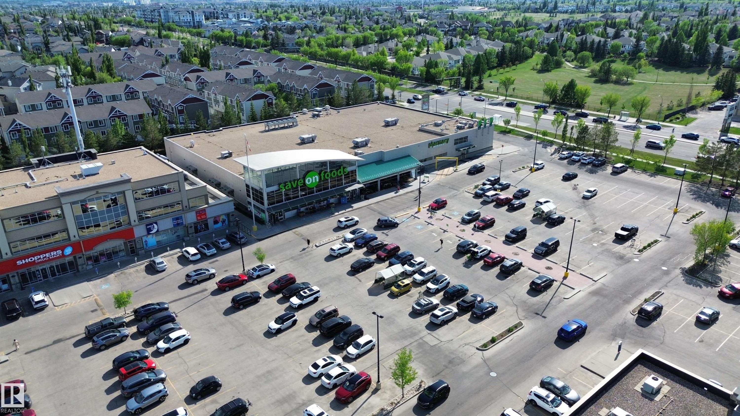Commercial complex featuring a large surface parking lot, retail storefronts, and a grocery store - 117 160 Magrath Road, Edmonton, AB - With View