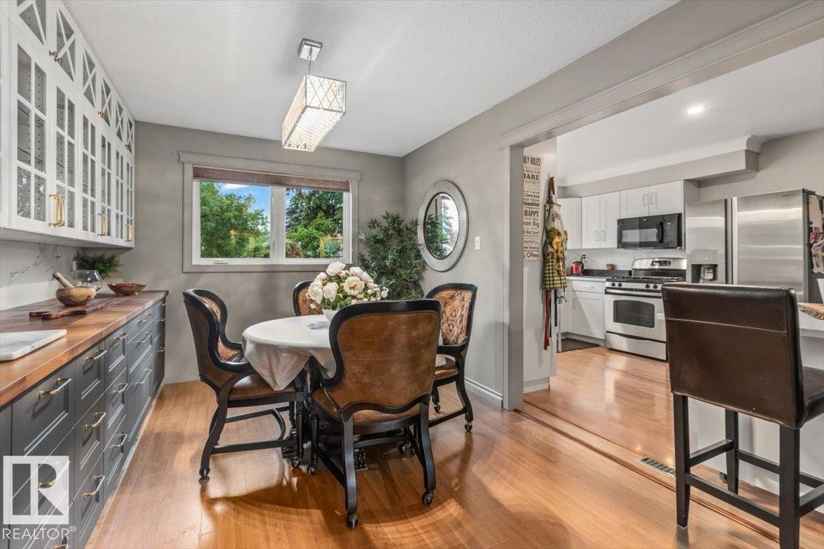 Dining area with wood-finish flooring, a window offering exterior views, and a linear chandelier - 6720 29 Avenue, Edmonton, AB