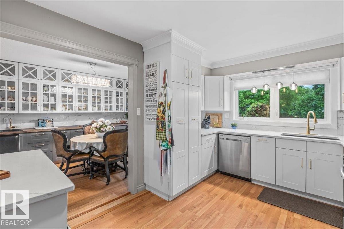 Bright kitchen featuring white cabinetry, stainless steel appliances, a window over the sink, wood-finish flooring, and a quartz countertop - 6720 29 Avenue, Edmonton, AB