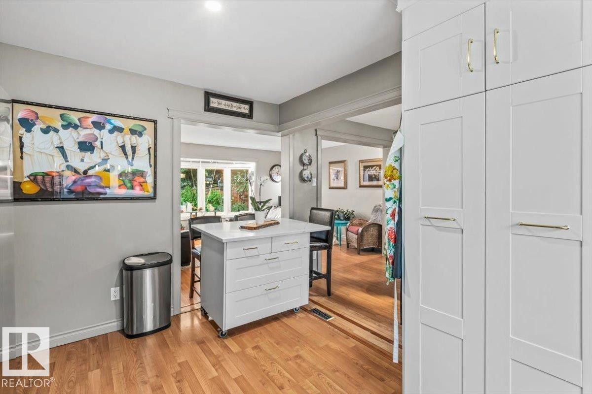 Kitchen featuring wood-finish flooring, a white mobile island with a stone-finish countertop, and white shaker-style cabinetry with gold-tone hardware - 6720 29 Avenue, Edmonton, AB