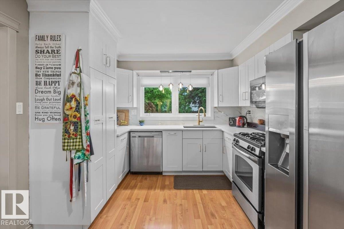 Contemporary kitchen featuring white cabinetry, stainless steel appliances, wood-finish flooring, white countertops, and a window above the sink - 6720 29 Avenue, Edmonton, AB