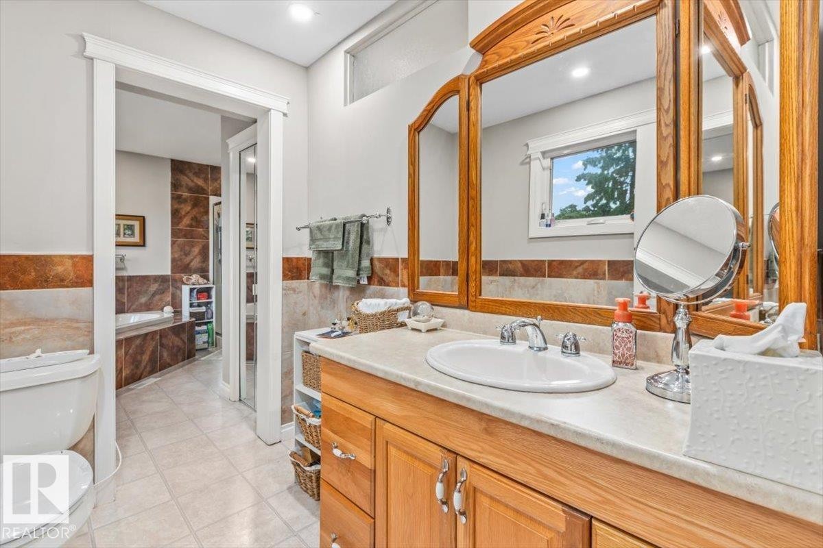 Bathroom featuring a light-toned vanity with an integrated sink and chrome faucet, custom wood-framed mirrors, and a window providing natural light - 6720 29 Avenue, Edmonton, AB