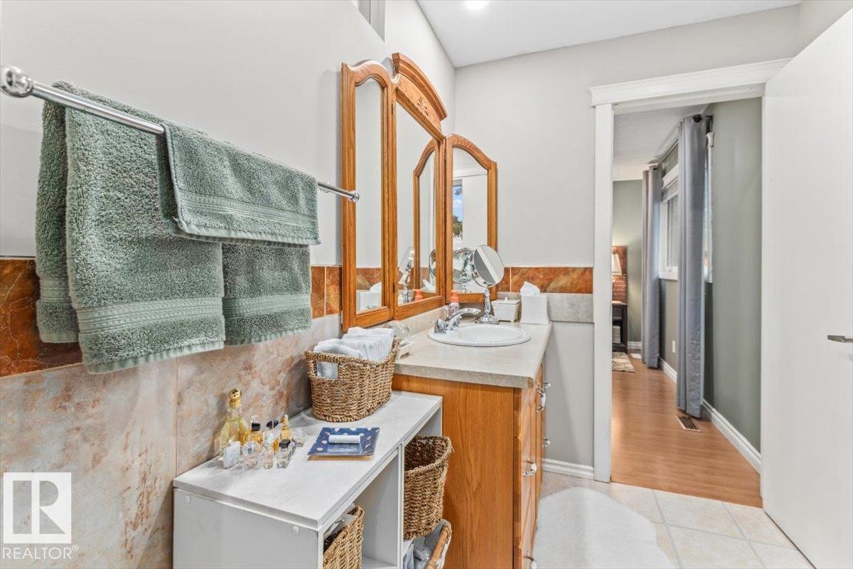 Bathroom featuring a single vanity with a laminate countertop, integrated sink, and wood-finish cabinetry - 6720 29 Avenue, Edmonton, AB