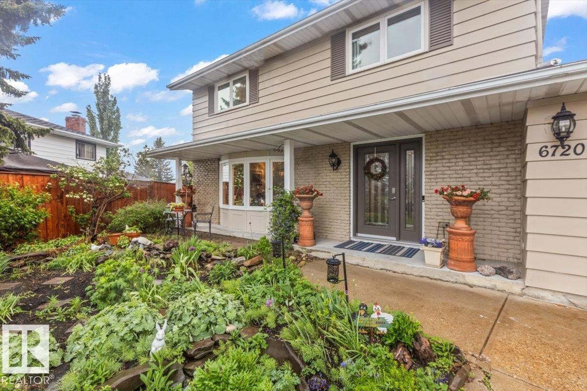 Exterior featuring tan siding, brick accents, a covered front entry with double doors, a bay window, and a terraced front garden - 6720 29 Avenue, Edmonton, AB