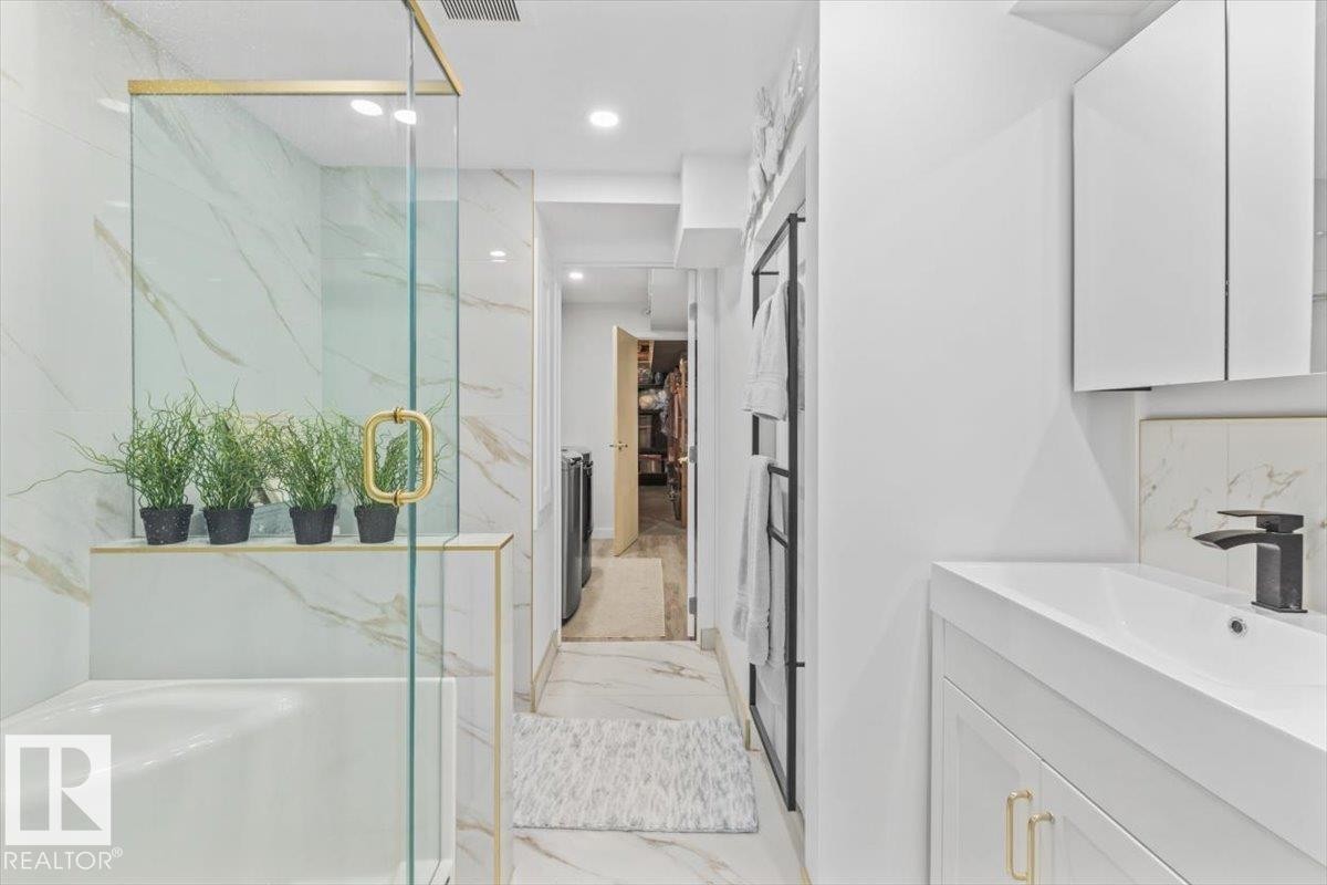 Modern bathroom featuring a glass-enclosed shower with gold-finish hardware, white marble-style wall tiling, and a built-in tub - 6720 29 Avenue, Edmonton, AB