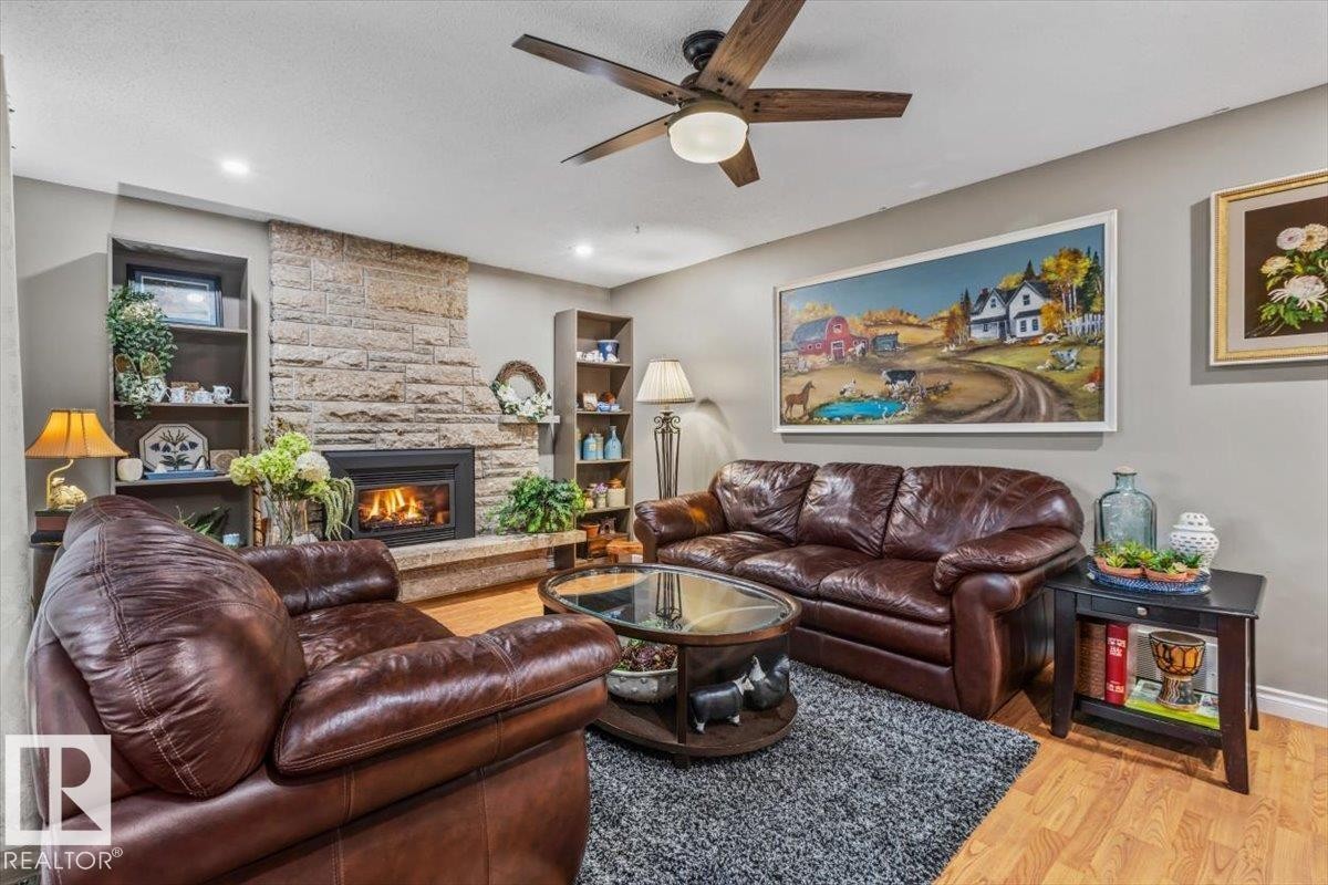 Stone-clad fireplace with a raised hearth, wood-finish flooring, recessed lighting, built-in shelving, and a ceiling fan - 6720 29 Avenue, Edmonton, AB