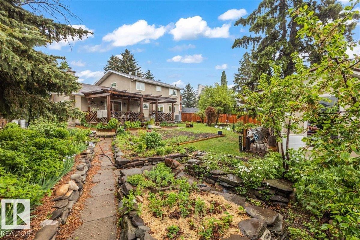 Expansive backyard featuring a stone pathway, multiple garden beds with rock borders, and mature perimeter trees - 6720 29 Avenue, Edmonton, AB