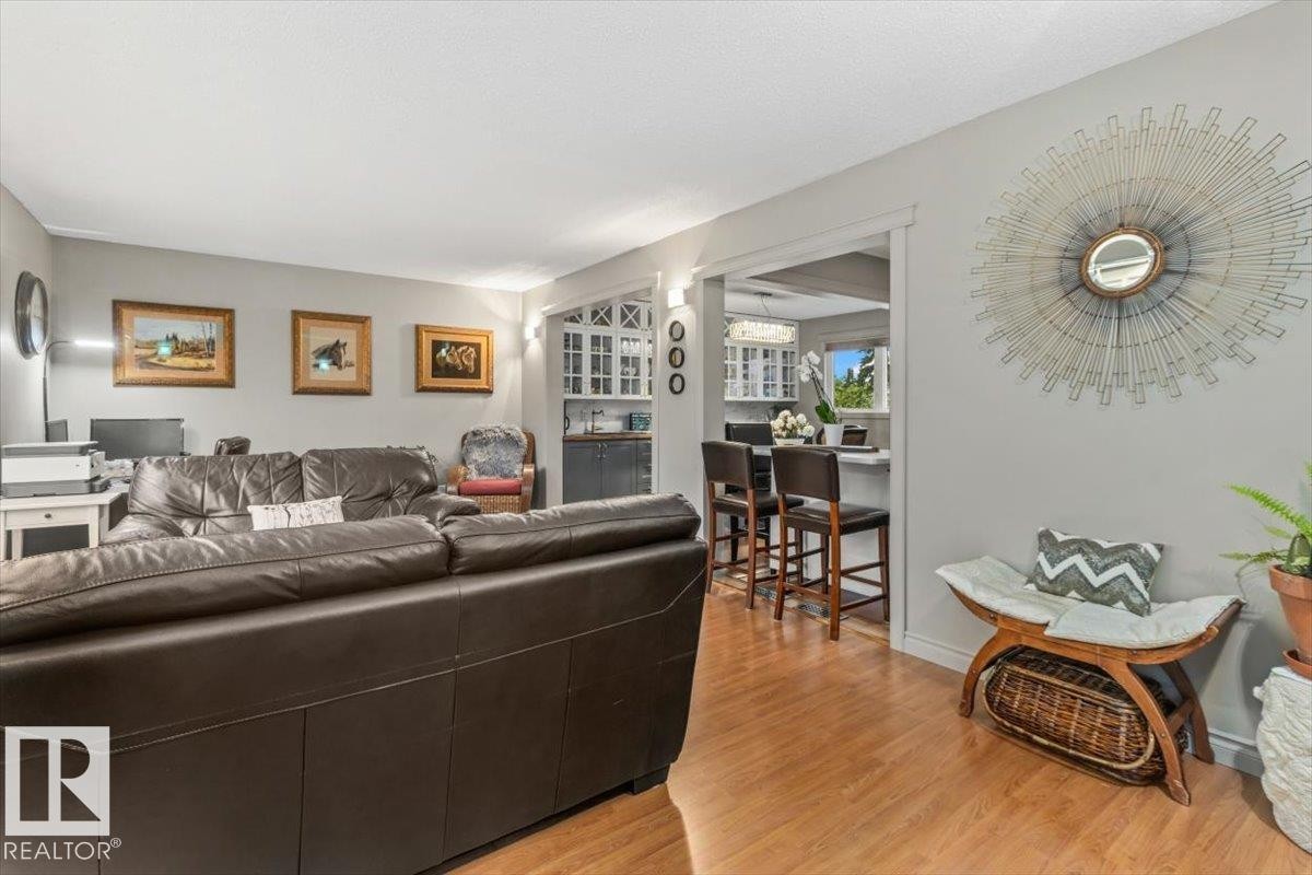 Light wood-finish flooring extending through the main living area, complemented by a wide entryway leading to a kitchen with white cabinetry and a breakfast bar - 6720 29 Avenue, Edmonton, AB