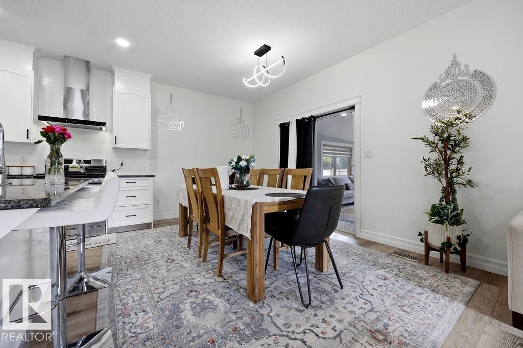 Open-concept kitchen and dining area featuring white cabinetry, dark countertops, wood-finish flooring, a contemporary chandelier, and a stainless steel range hood - 13703 166 Avenue Nw, Edmonton, AB - Indoor Photo Showing Dining Room