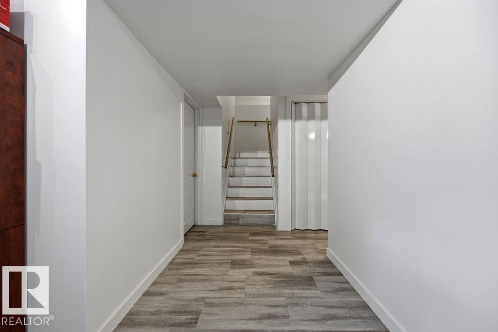 Hallway featuring wood-finish flooring, white painted walls, and a staircase with wood treads and a metal handrail - 13703 166 Avenue Nw, Edmonton, AB - Indoor Photo Showing Other Room