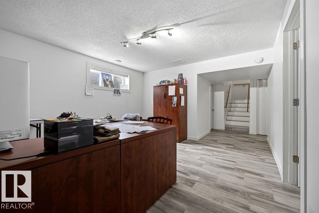 Spacious room featuring light wood-finish flooring, white walls, a track lighting fixture, and a window with horizontal blinds - 13703 166 Avenue Nw, Edmonton, AB - Indoor