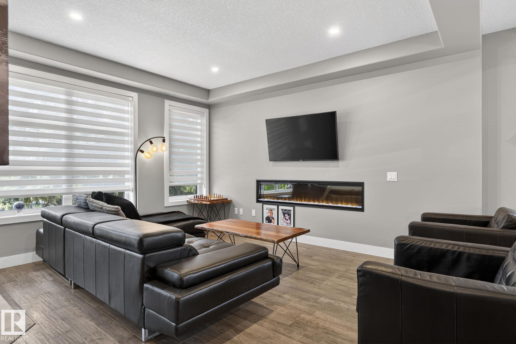 Living space featuring wood-finish flooring, a linear electric fireplace, recessed ceiling lighting, and a tray ceiling - 8809 148 Street, Edmonton, AB - Indoor Photo Showing Living Room With Fireplace