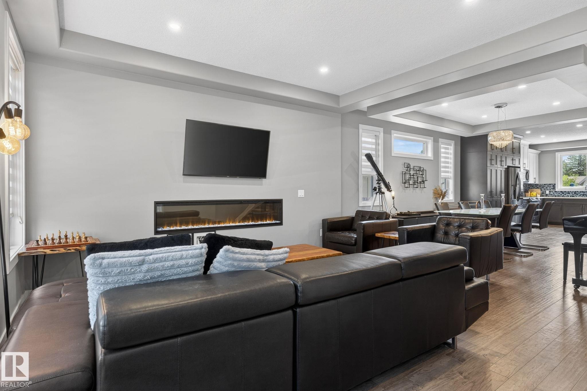 Spacious living area featuring wood-finish flooring, an electric fireplace with mounted television, and recessed lighting - 8809 148 Street, Edmonton, AB - Indoor Photo Showing Living Room With Fireplace