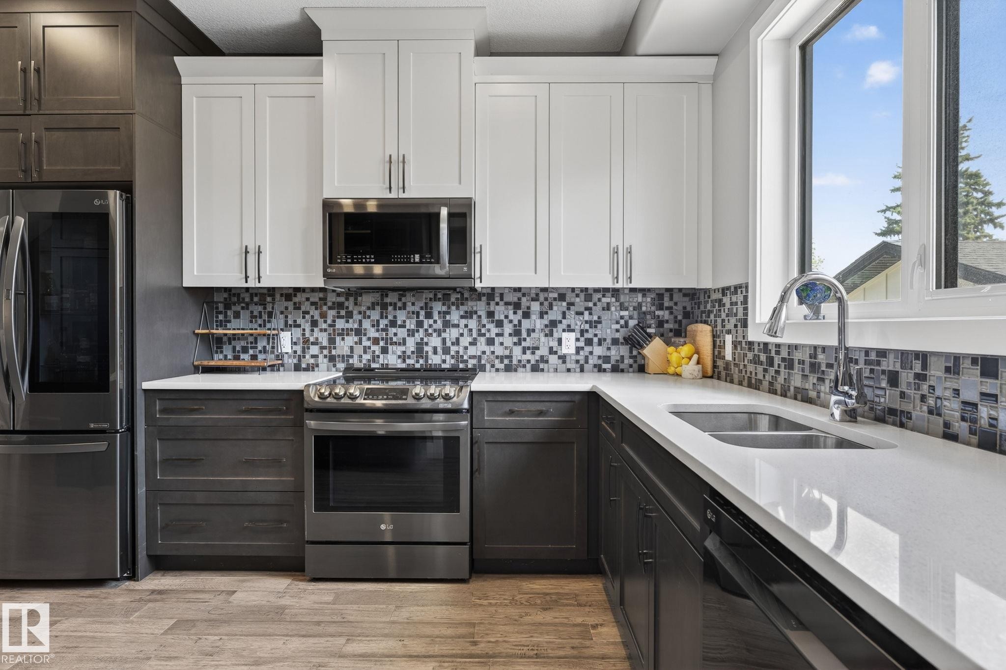 Contemporary kitchen featuring two-tone cabinetry, stainless steel appliances, a mosaic tile backsplash, and light-toned countertops - 8809 148 Street, Edmonton, AB - Indoor Photo Showing Kitchen With Double Sink With Upgraded Kitchen