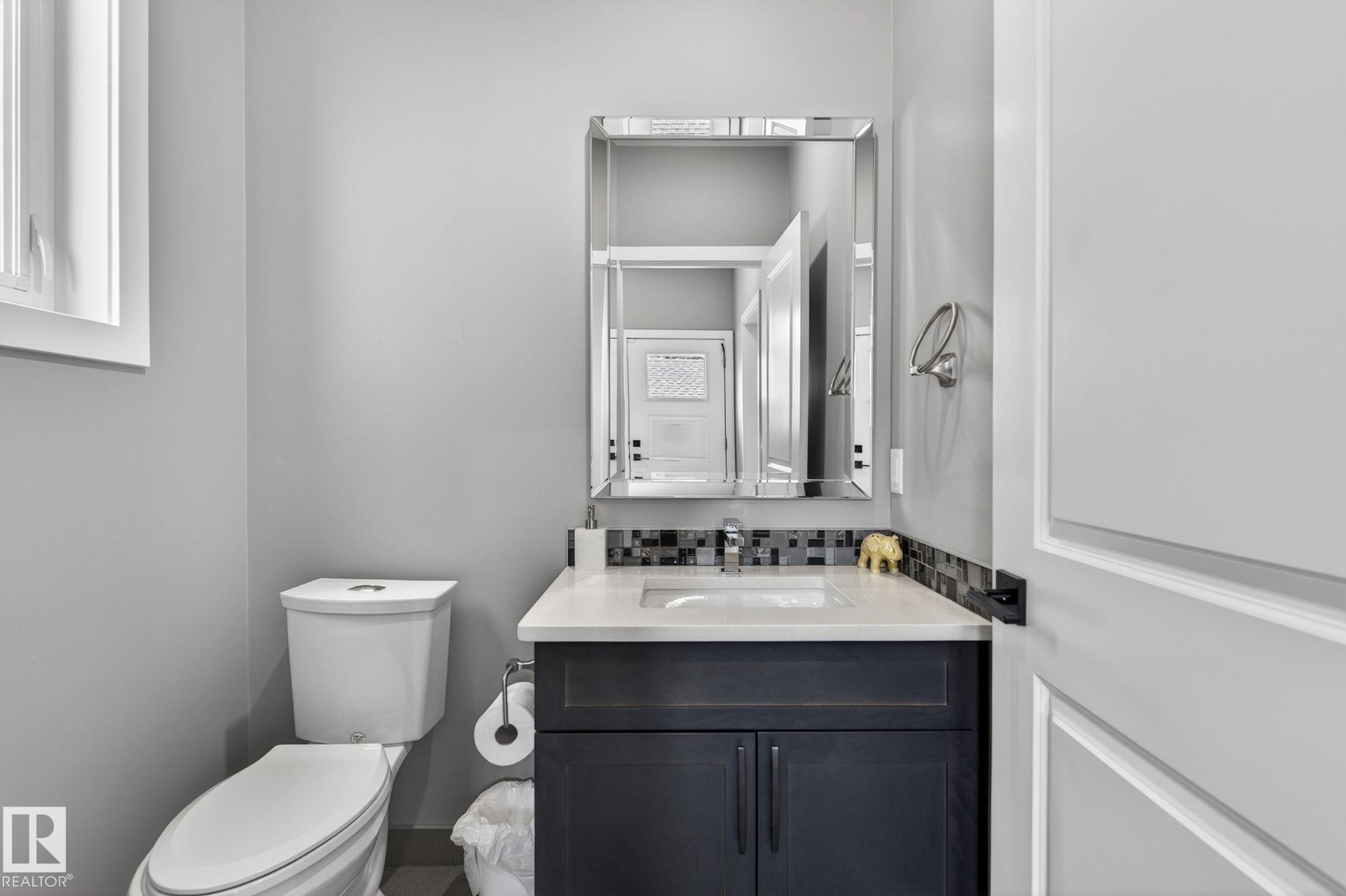 Powder room featuring a dark wood vanity with a white countertop, mosaic tile backsplash, and a contemporary mirror - 8809 148 Street, Edmonton, AB - Indoor Photo Showing Bathroom