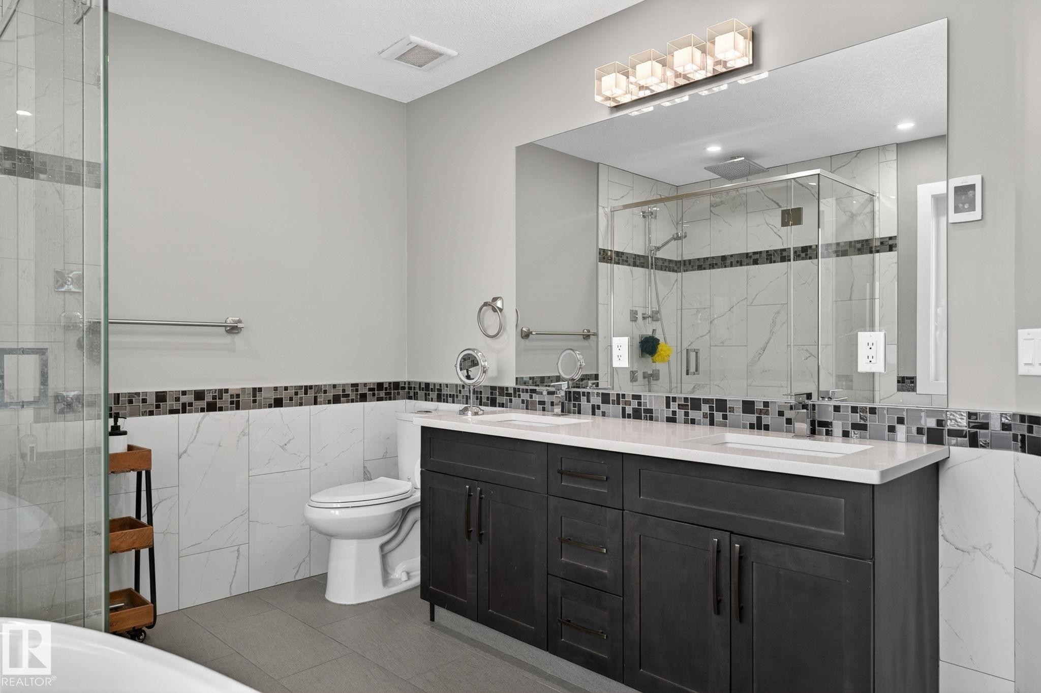 Contemporary bathroom featuring a dark wood double vanity with dual sinks, a large wall-mounted mirror, and a frameless glass-enclosed shower - 8809 148 Street, Edmonton, AB - Indoor Photo Showing Bathroom
